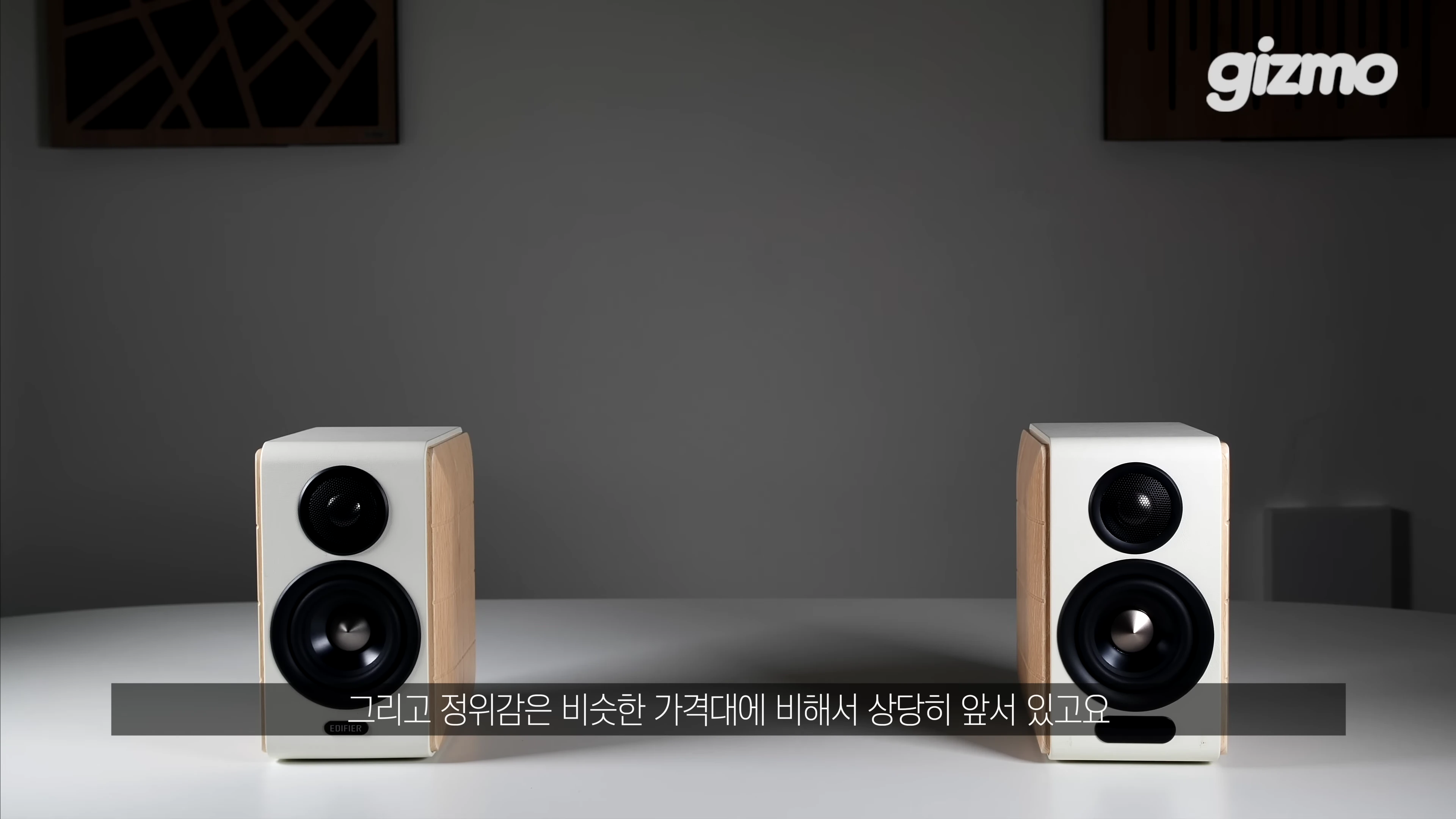 흰색과 나무 질감이 섞인 북쉘프 스피커 한 쌍이 테이블 위에 놓여 있는 모습