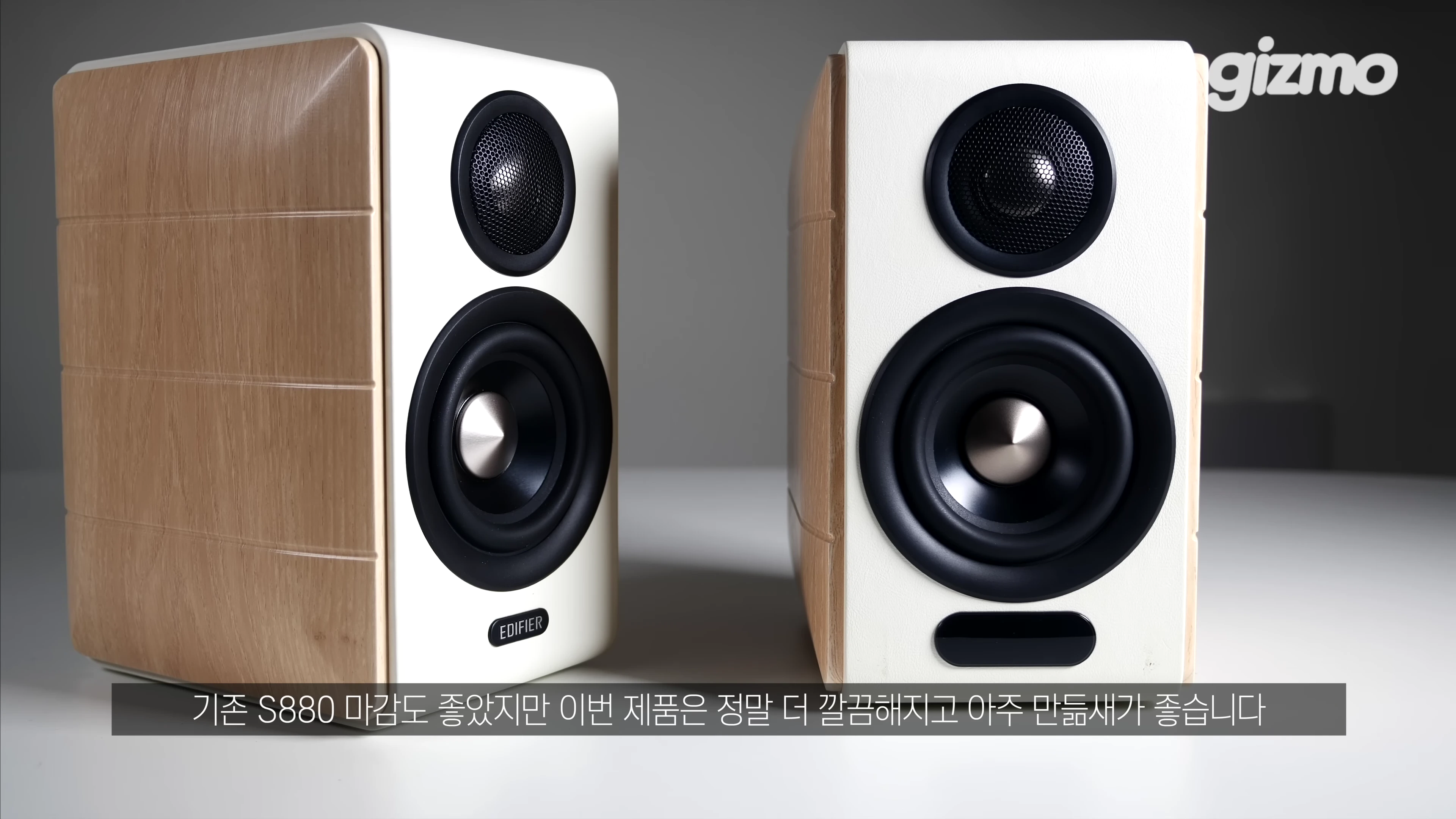 흰색 전면 패널과 밝은 나무 무늬 측면이 조화를 이루는 2채널 북쉘프 스피커 한 쌍이 밝은 배경 앞에 놓여 있다.