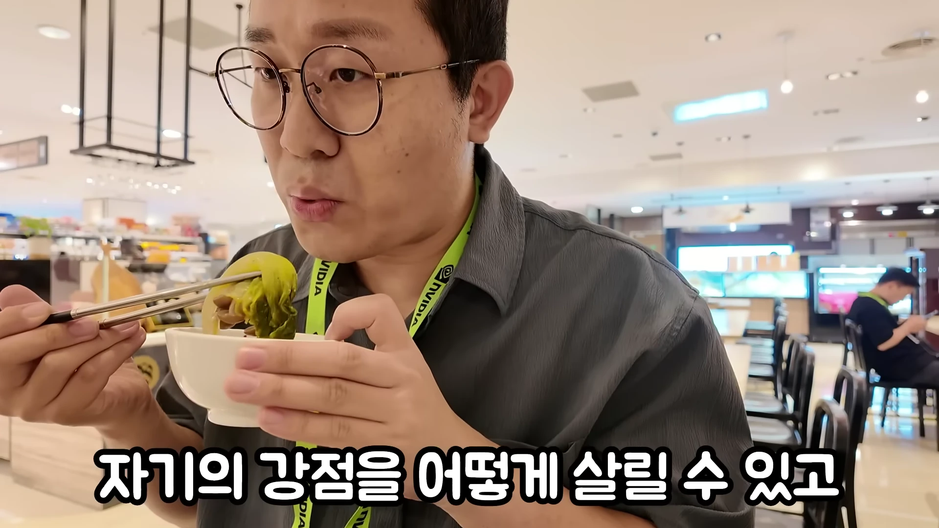안경을 쓴 남성이 엔비디아 로고가 새겨진 목걸이를 걸고 식당에서 음식을 먹고 있는 모습