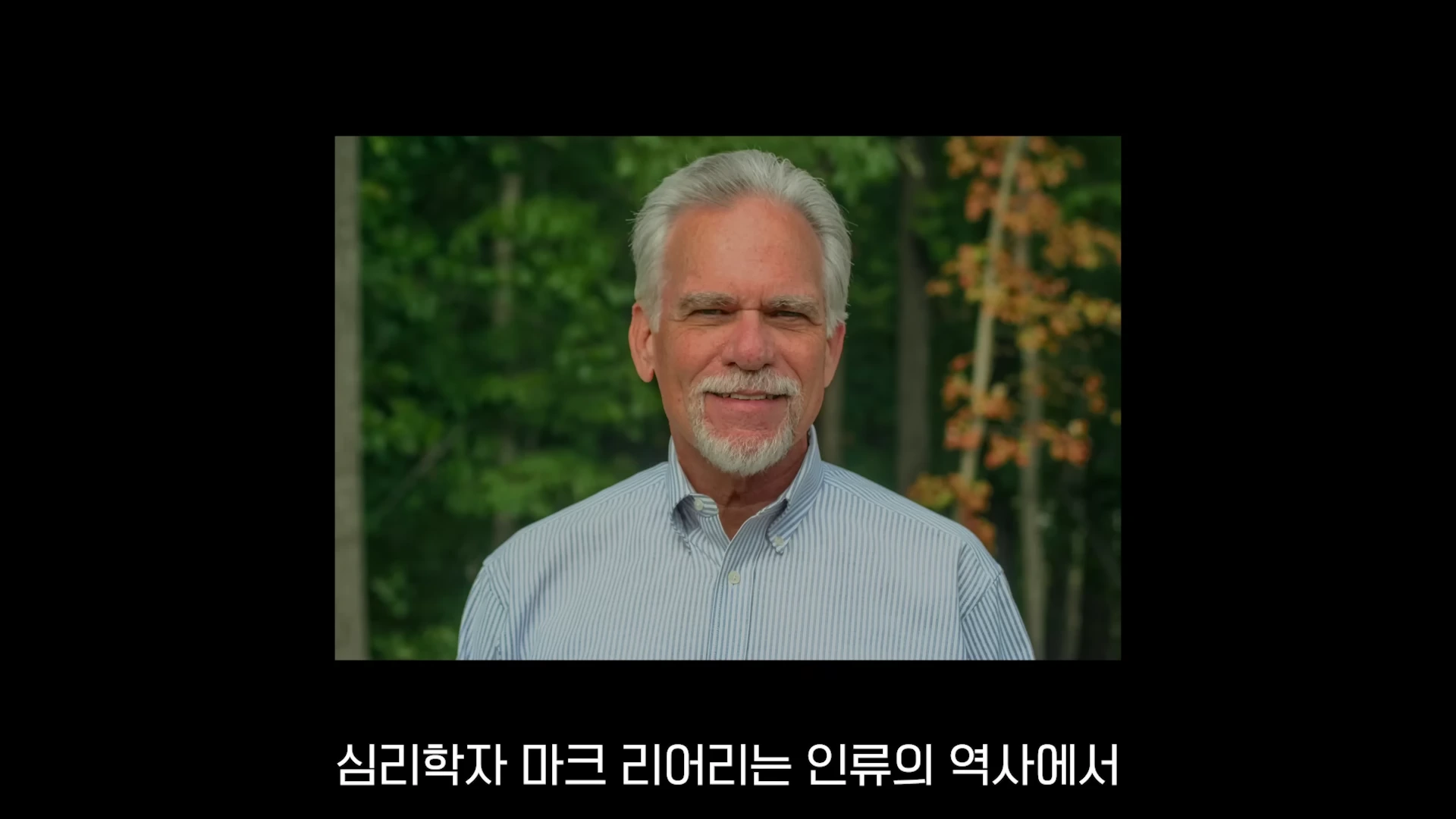 흰 머리와 수염을 가진 중년 남성이 숲을 배경으로 정면을 바라보고 있다.