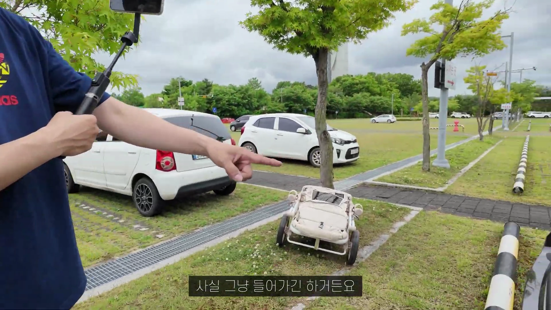 야외 주차장에서 한 남성이 손가락으로 유모차를 가리키고 있는 모습