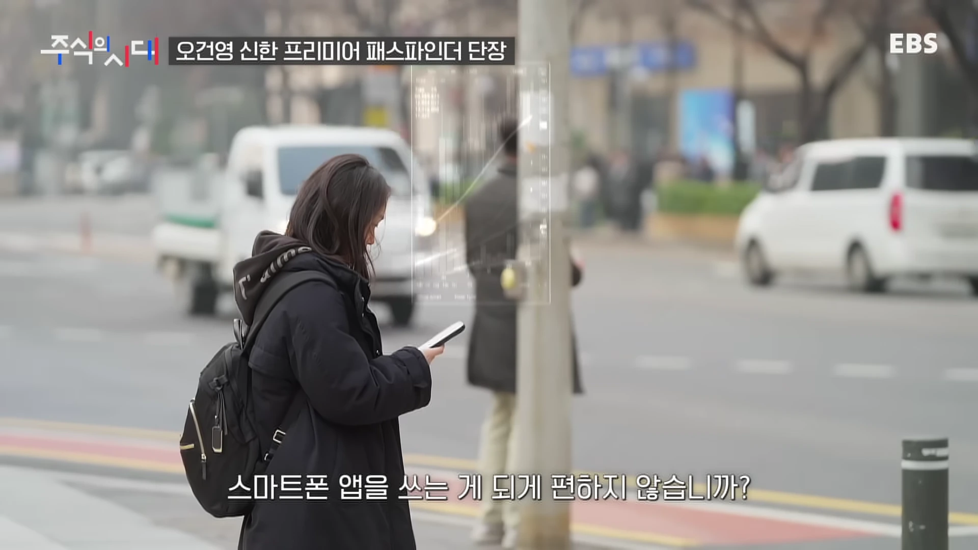 길거리에서 스마트폰을 보는 사람과 그 옆에 떠 있는 주식 차트 그래픽