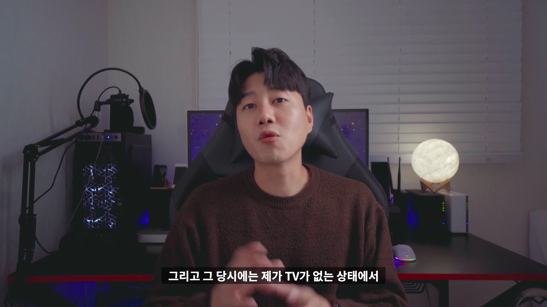 실내 책상 앞에 앉아 카메라를 보며 이야기하는 남성