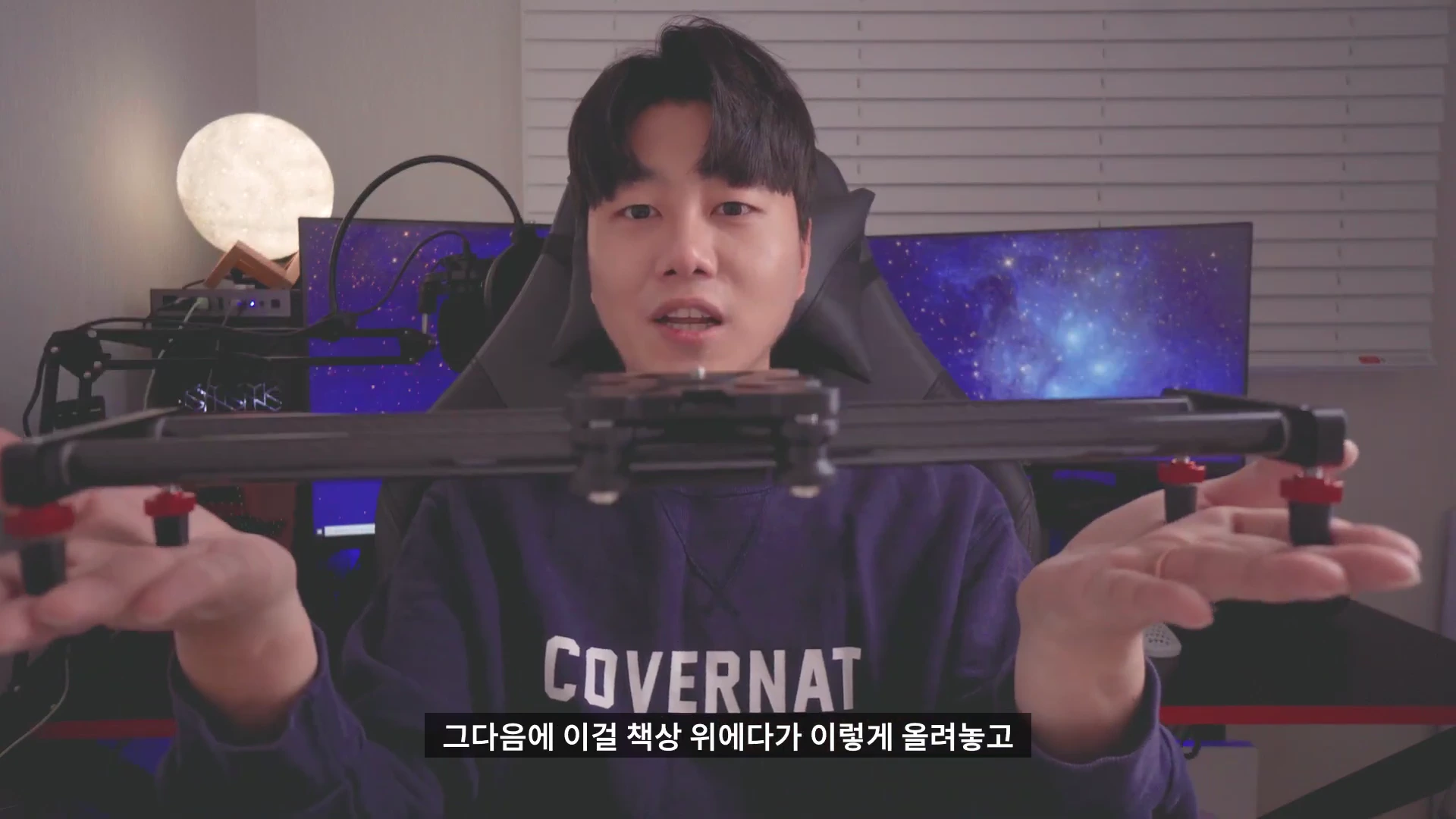 한 남성이 양손으로 검은색 카메라 슬라이더를 들어 보이며 설명하고 있다.