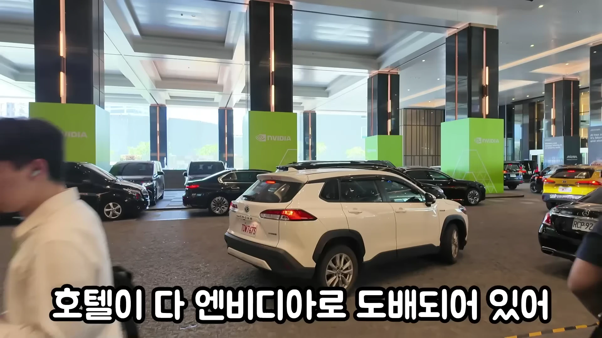 엔비디아 로고가 새겨진 녹색 기둥들이 세워진 호텔 로비에 차량들이 줄지어 서 있는 모습
