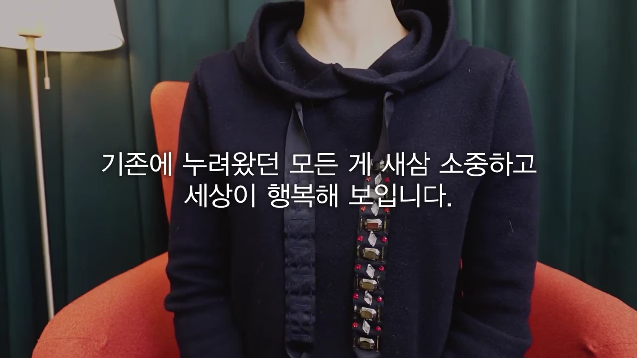 검은색 후드티를 입고 주황색 의자에 앉아 있는 사람의 상반신과 화면 중앙의 자막.