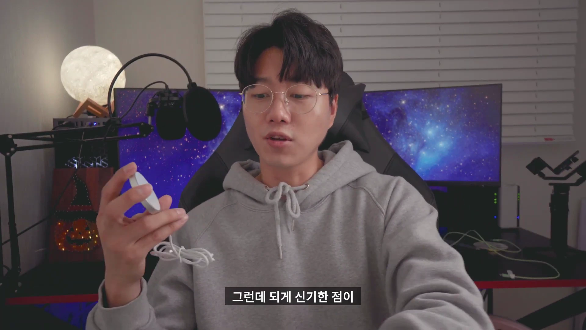 안경을 쓴 남성이 방 안에서 무선 충전기를 손에 들고 설명하고 있다.