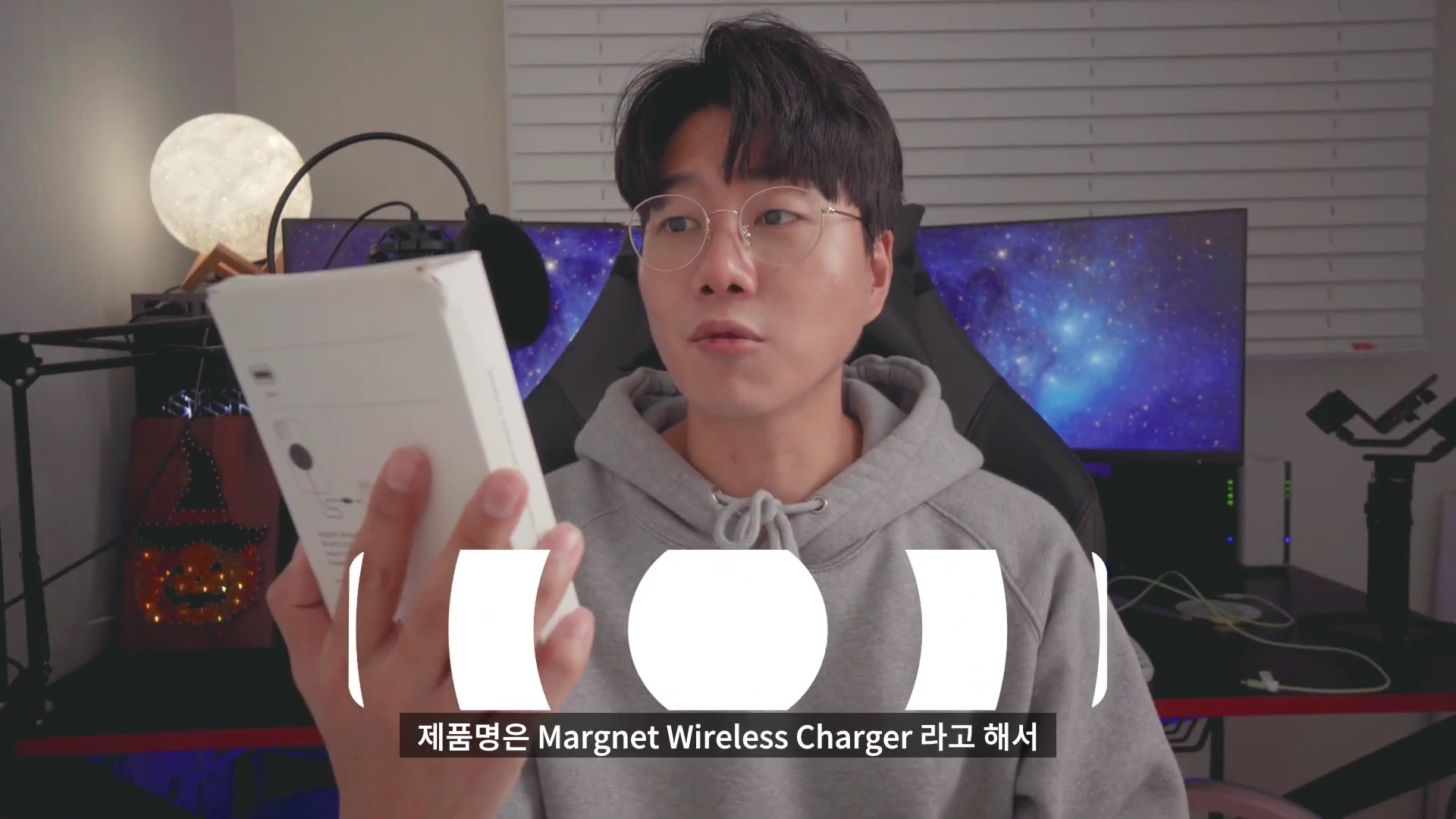 안경을 쓴 남성이 카메라를 보며 흰색 무선 충전기 제품 상자를 들어 보이고 있다.