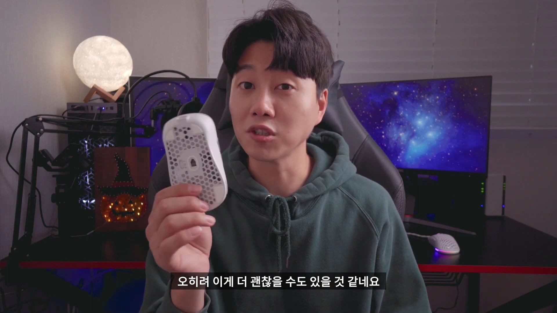 게이밍 룸을 배경으로 한 남성이 구멍이 뚫린 타공형 무선 마우스를 손에 들고 설명하고 있다.