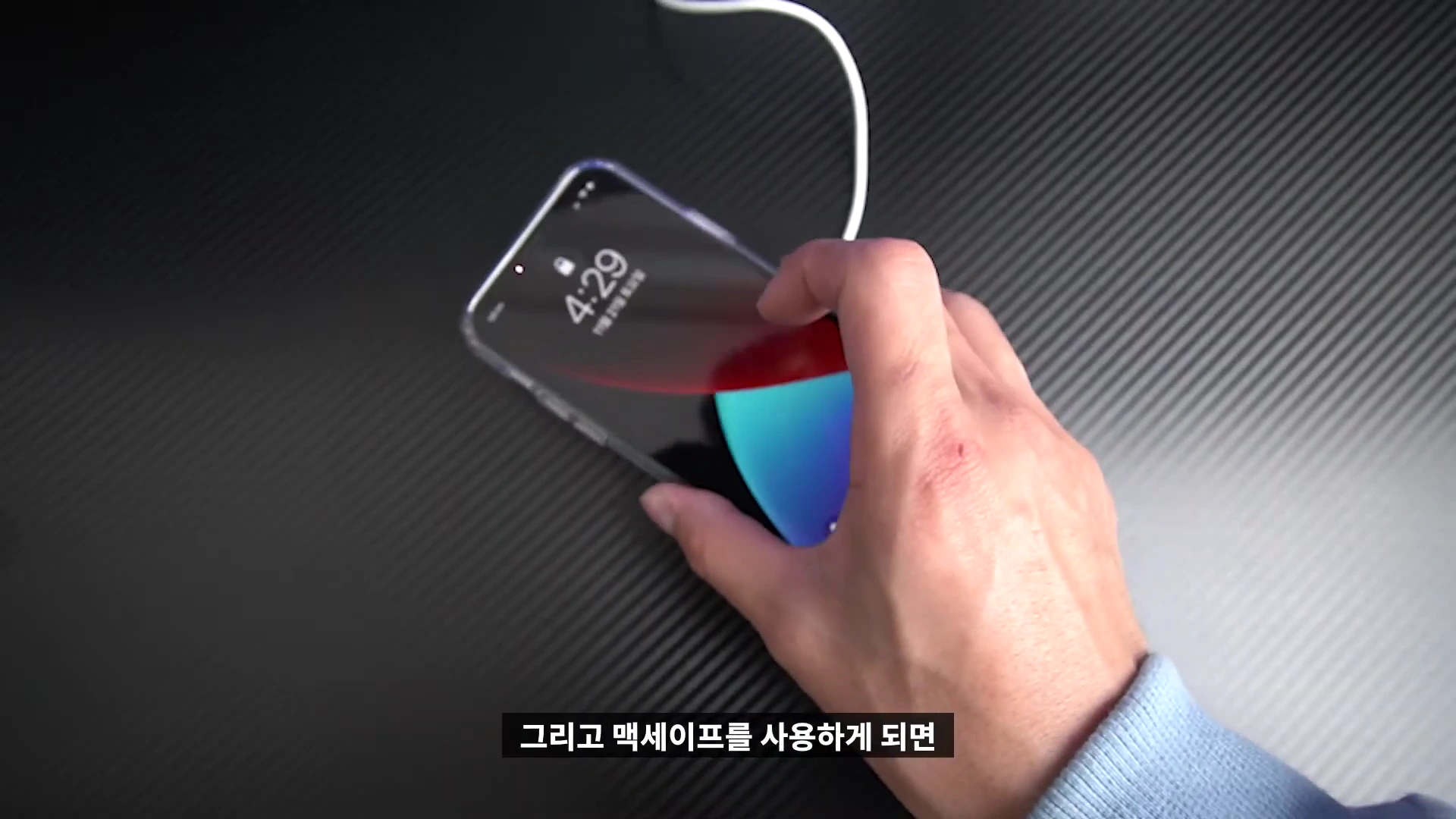 투명 케이스를 씌운 스마트폰을 맥세이프 충전기에 부착하는 손의 모습