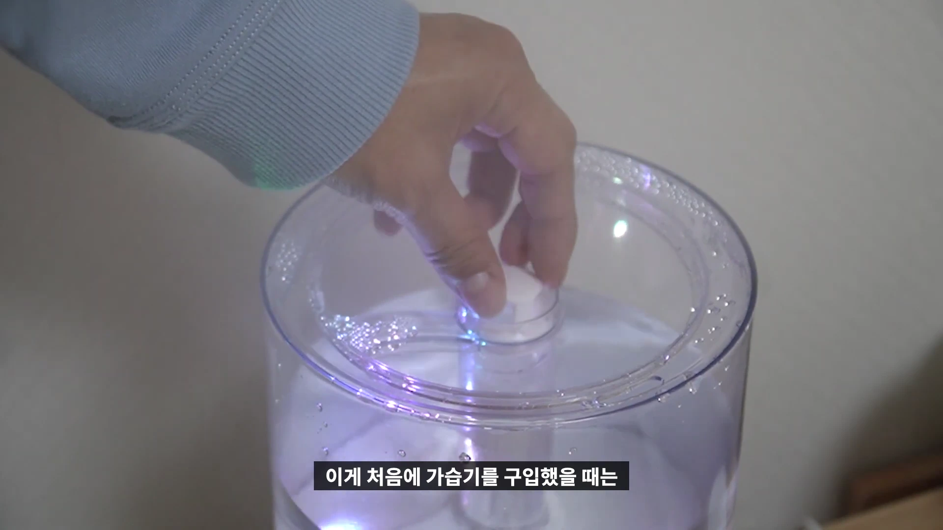 투명한 가습기 물통 뚜껑을 손으로 열고 있는 모습