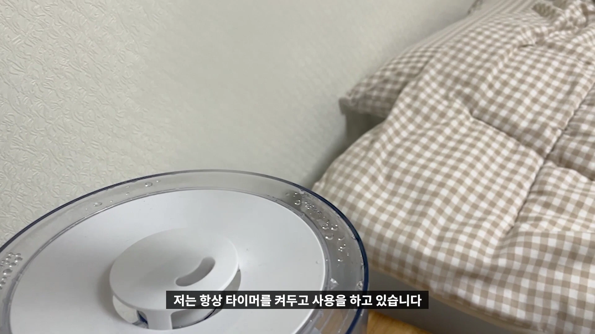 침대 옆에 놓인 흰색 가습기 상단부와 물방울이 맺힌 투명한 물통의 모습