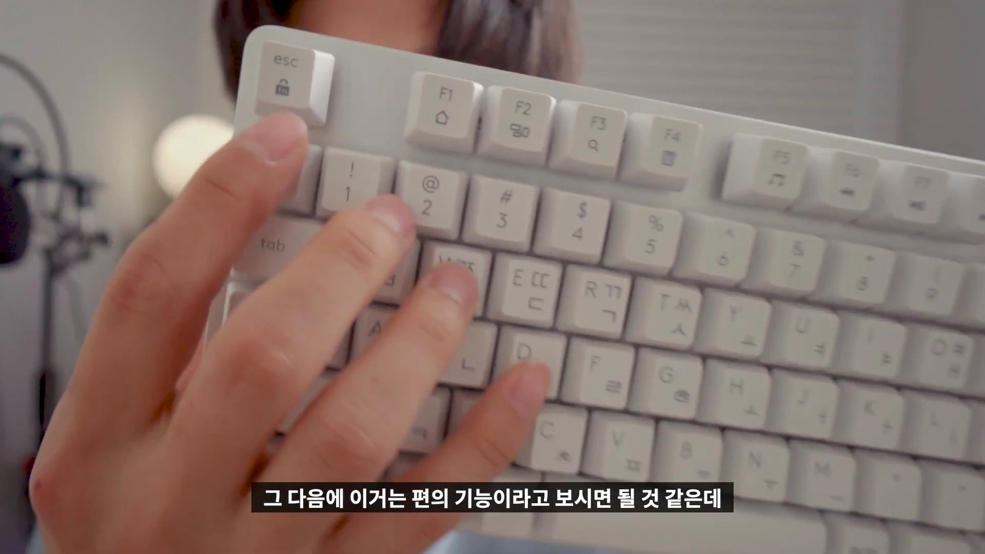 손으로 화이트 기계식 키보드의 상단 기능 키 부분을 가리키는 모습