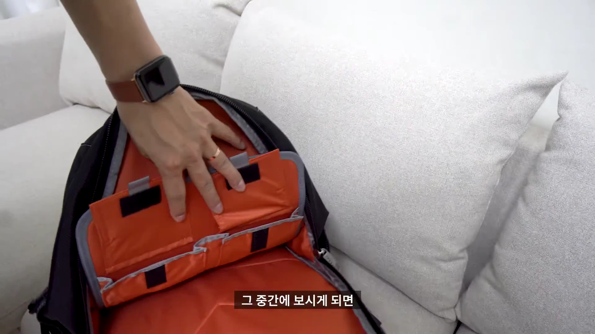 백팩 내부의 주황색 수납 공간을 손으로 가리키며 보여주는 모습