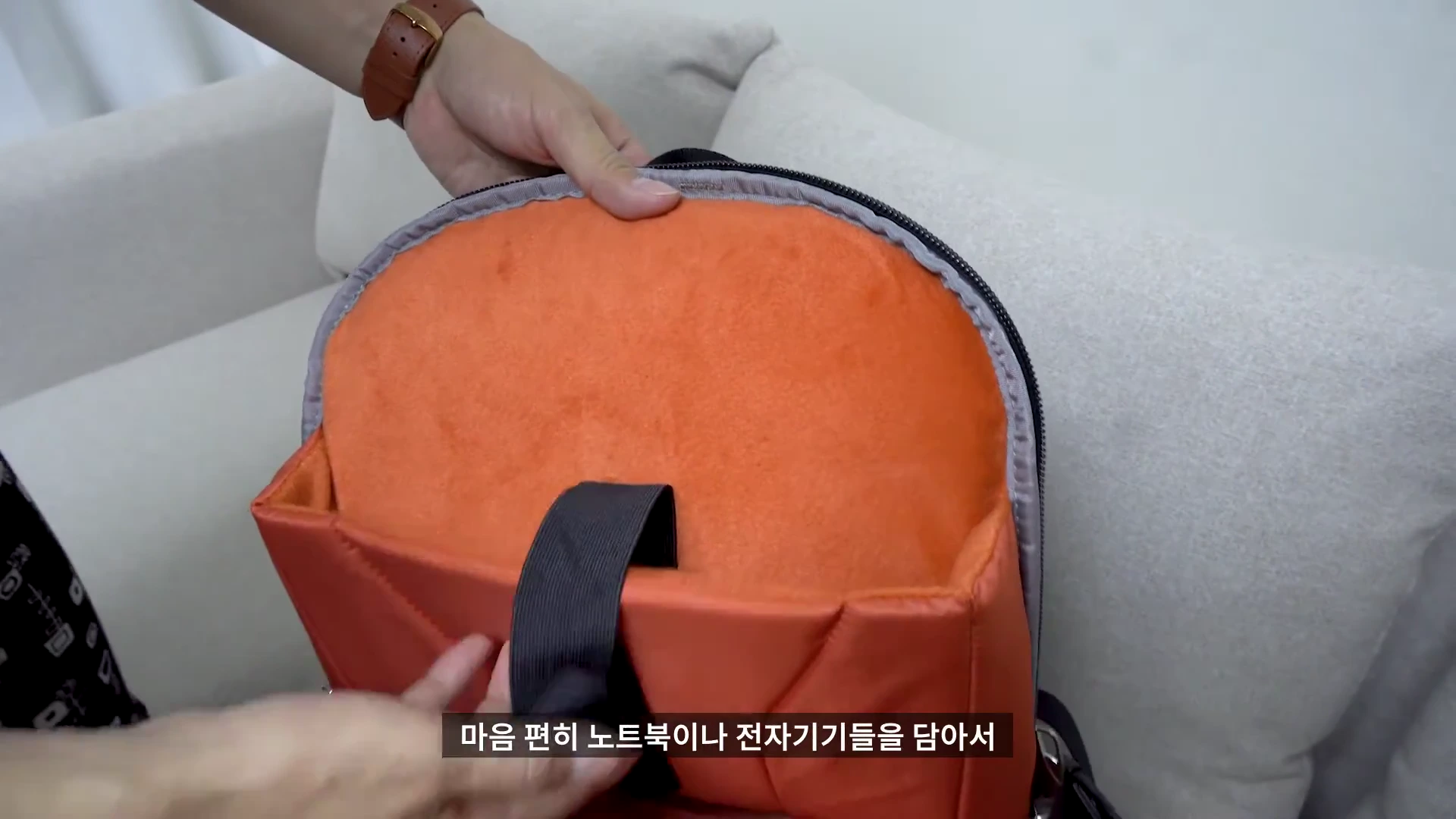 밝은 주황색 안감이 돋보이는 백팩 내부의 노트북 수납 공간을 손으로 보여주는 모습