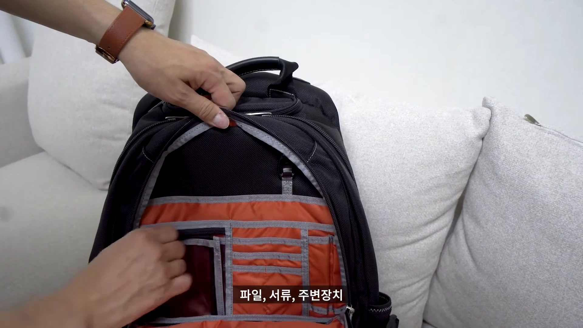 검은색 백팩의 전면 포켓을 열어 내부의 오렌지색 수납공간을 보여주는 모습