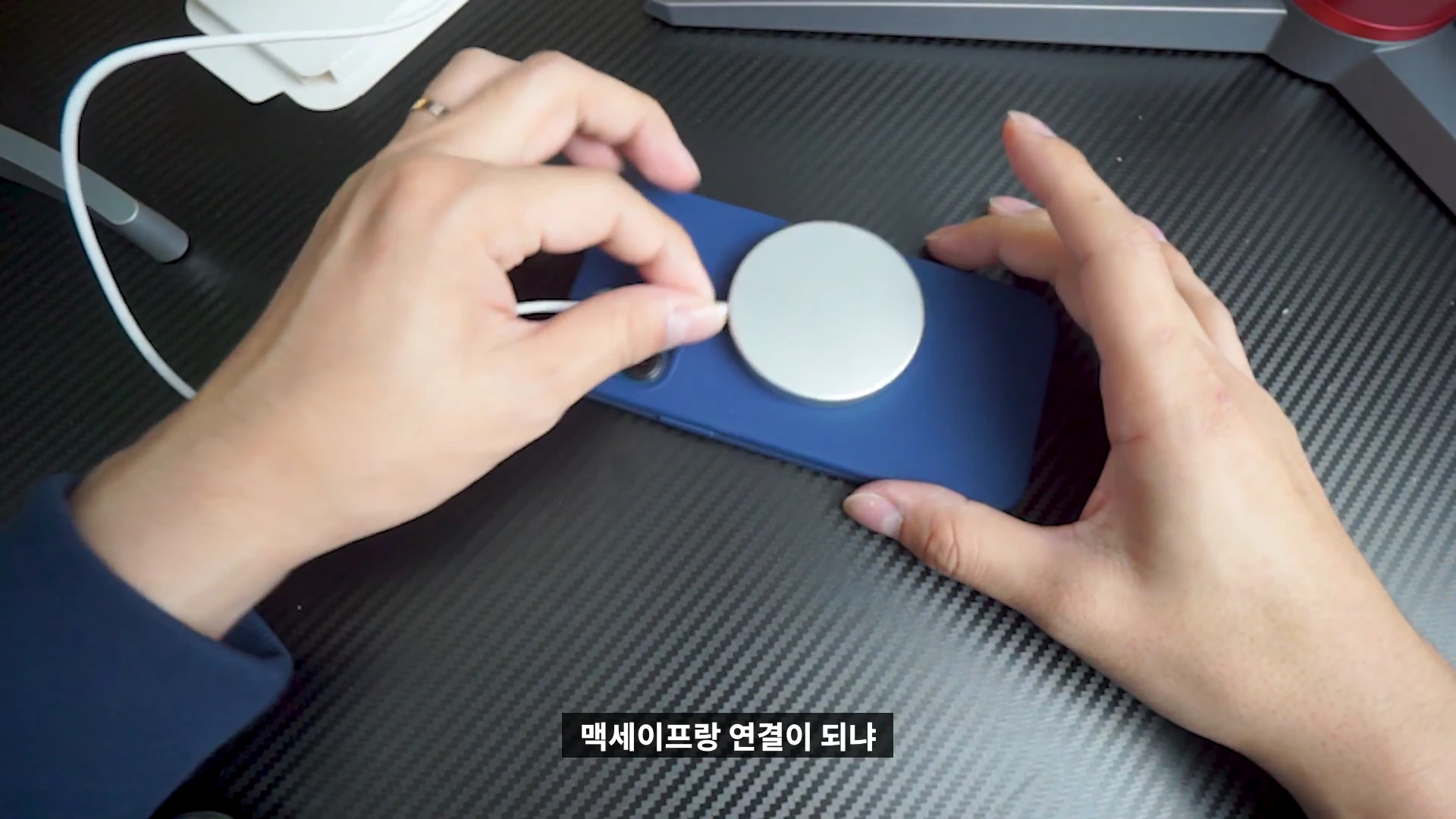 파란색 실리콘 케이스를 씌운 스마트폰 뒷면에 맥세이프 충전기를 부착하는 모습