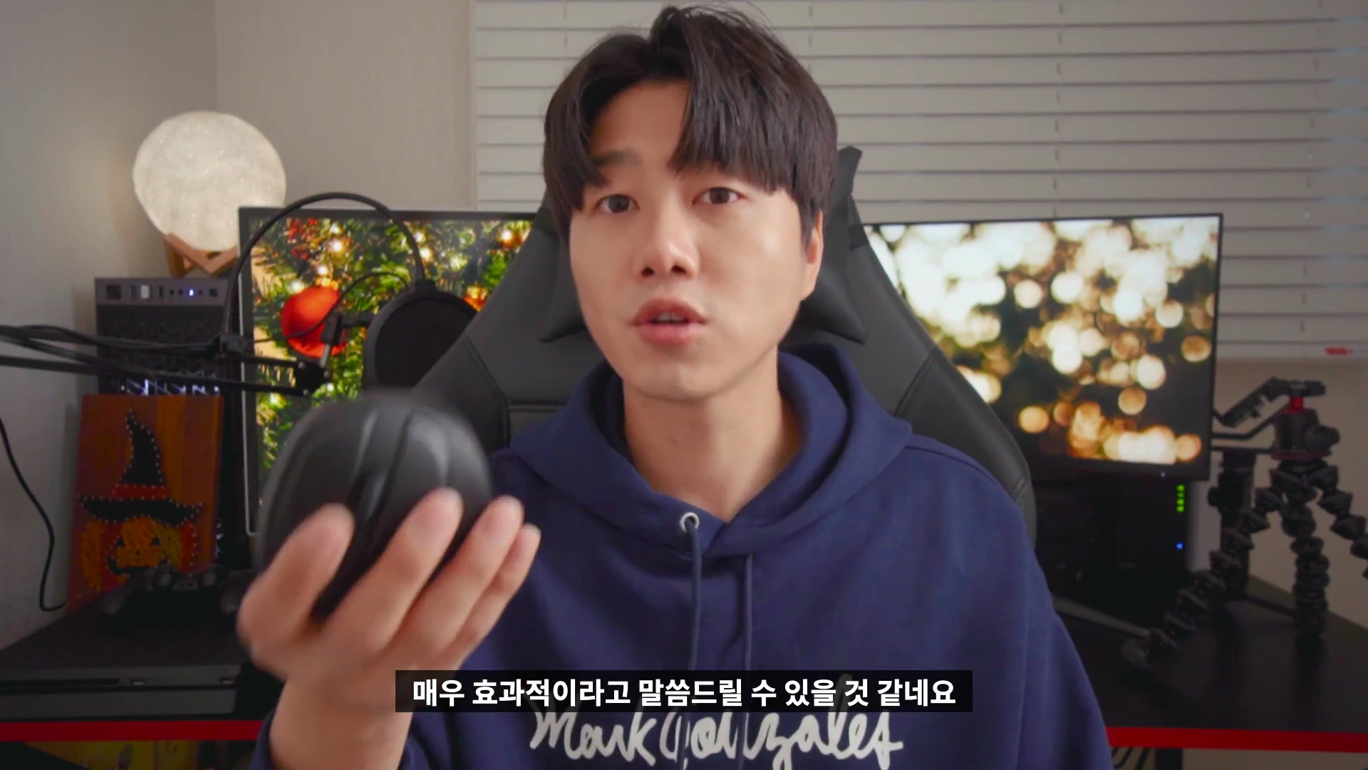 한 남성이 검은색 버티컬 마우스를 손에 들고 카메라를 보며 설명하는 모습