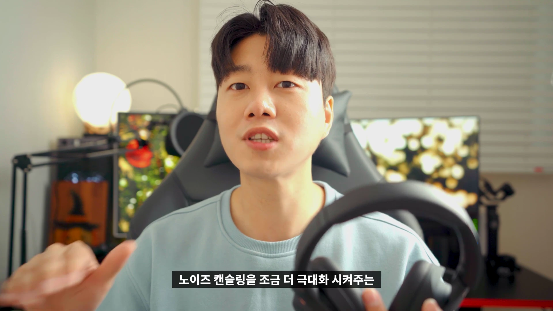 헤드폰을 손에 들고 설명하는 남성이 카메라를 응시하고 있다.