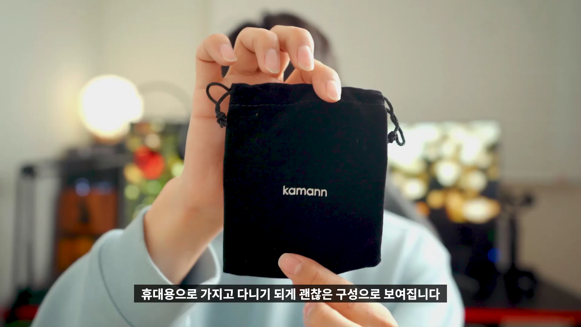 한 사람이 브랜드 로고가 새겨진 검은색 파우치를 손으로 들어 보이고 있다.
