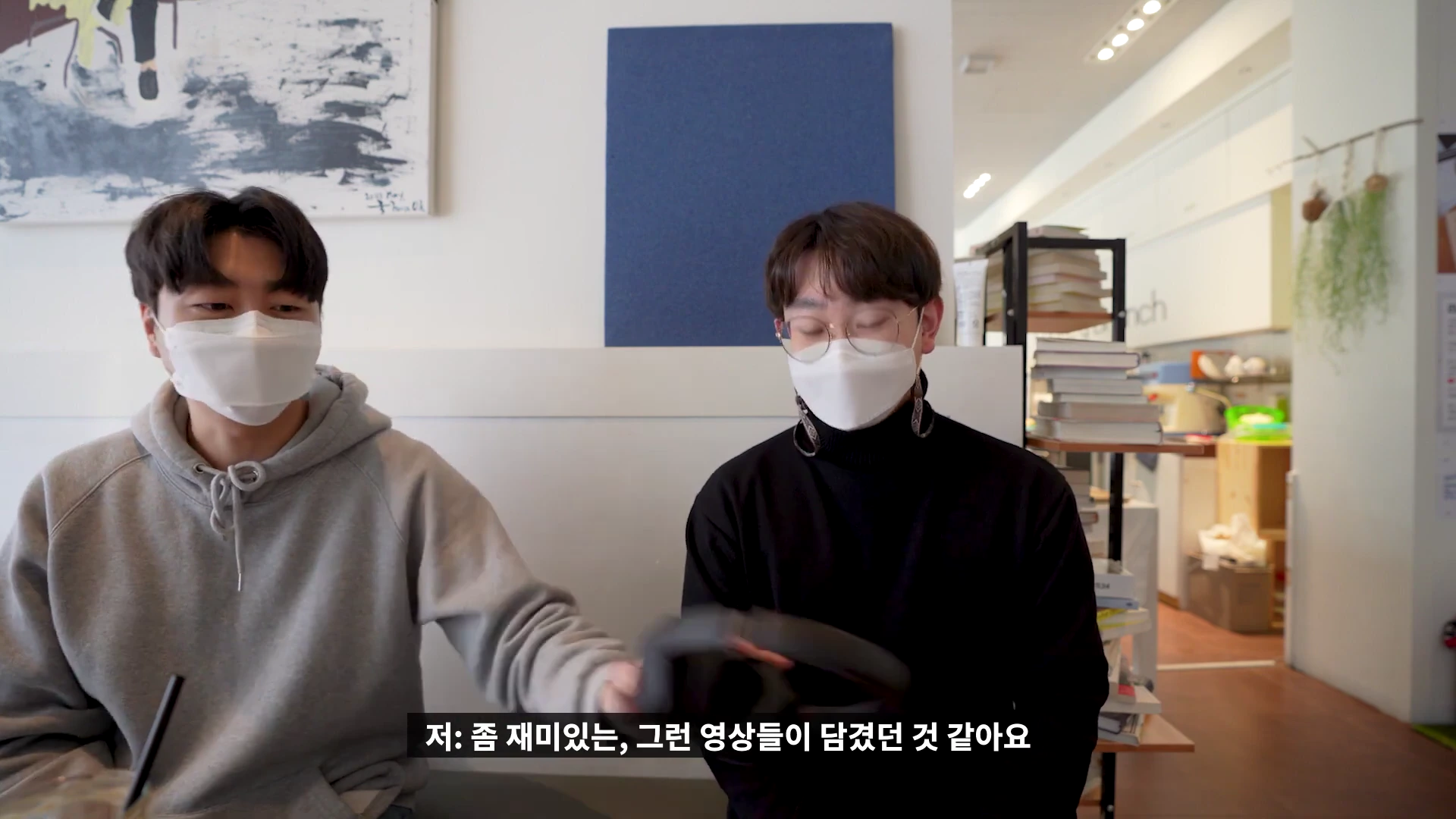 마스크를 쓴 두 남성이 실내에서 헤드폰을 주고받으며 대화를 나누는 모습