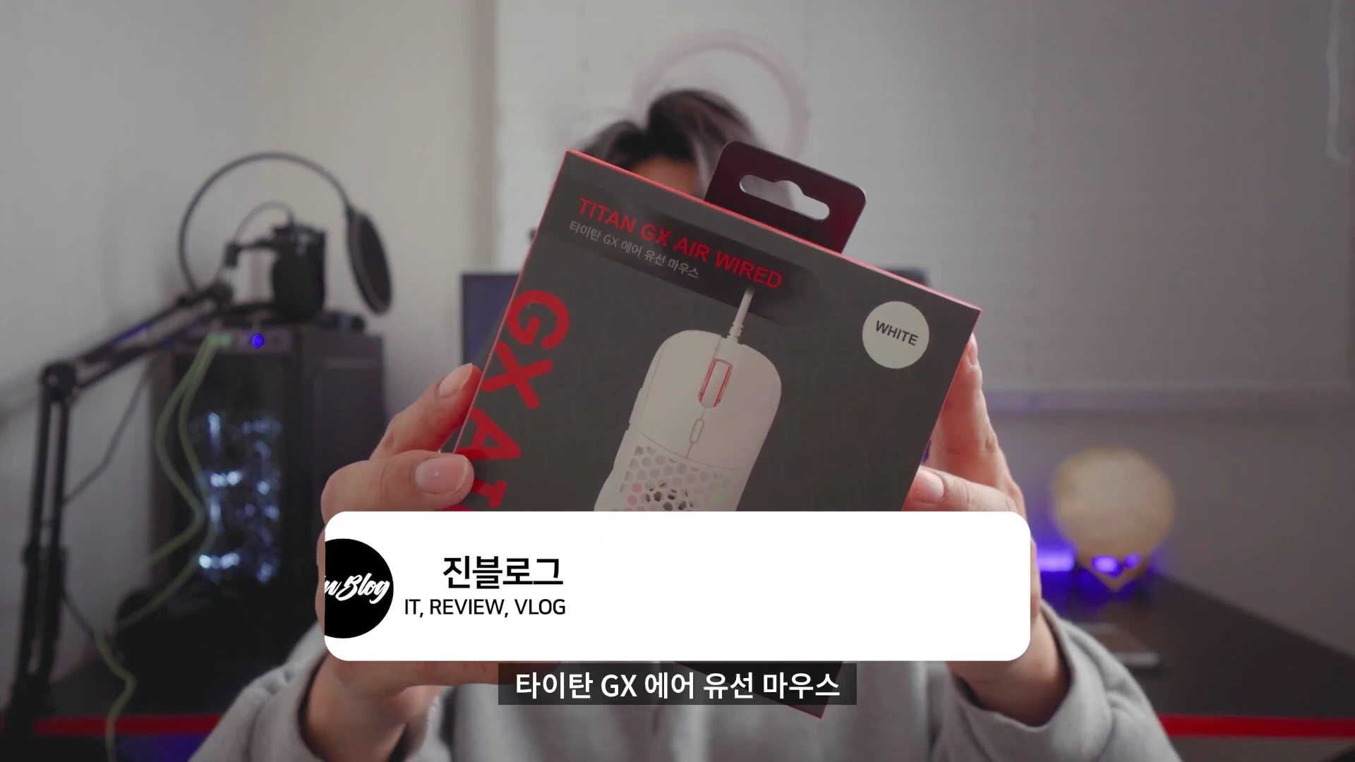 한 남성이 카메라를 향해 제닉스 타이탄 GX 에어 유선 마우스 제품 상자를 들어 보이고 있다.