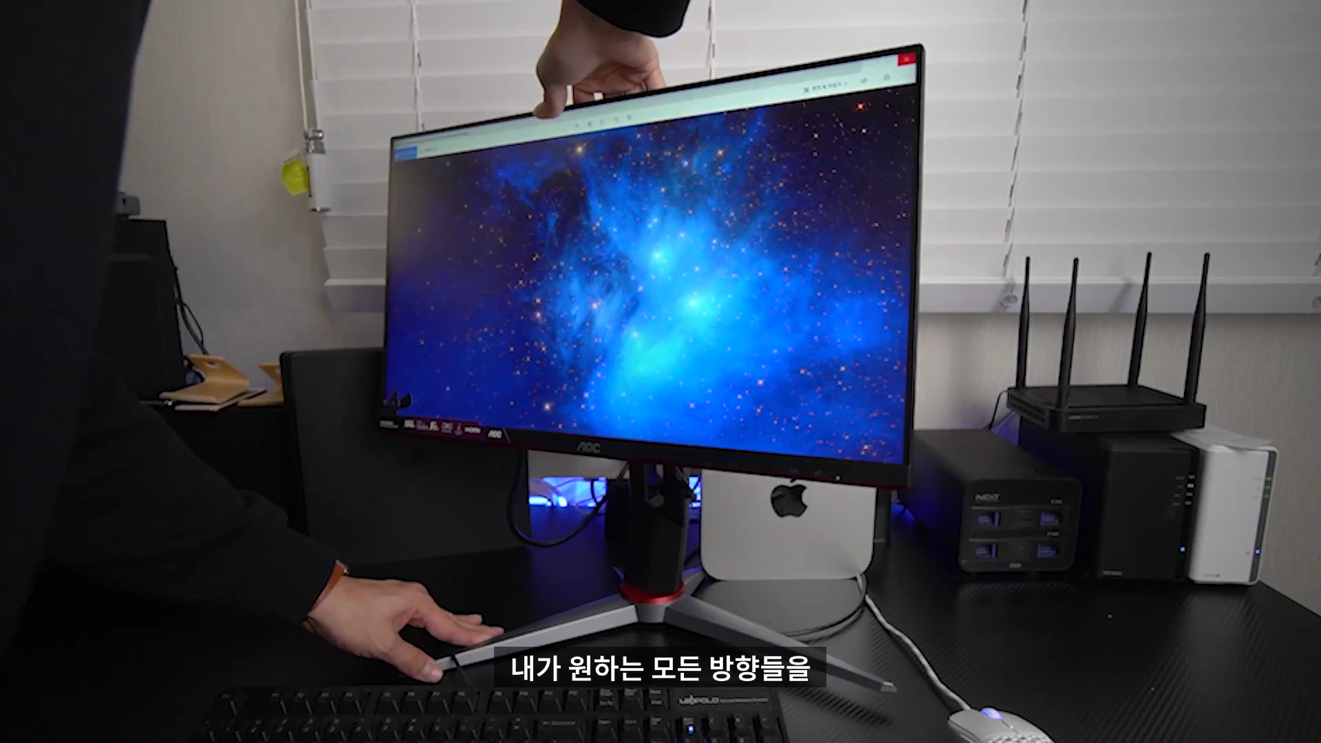 책상 위에서 사용자가 모니터의 높이와 각도를 조절하고 있는 모습