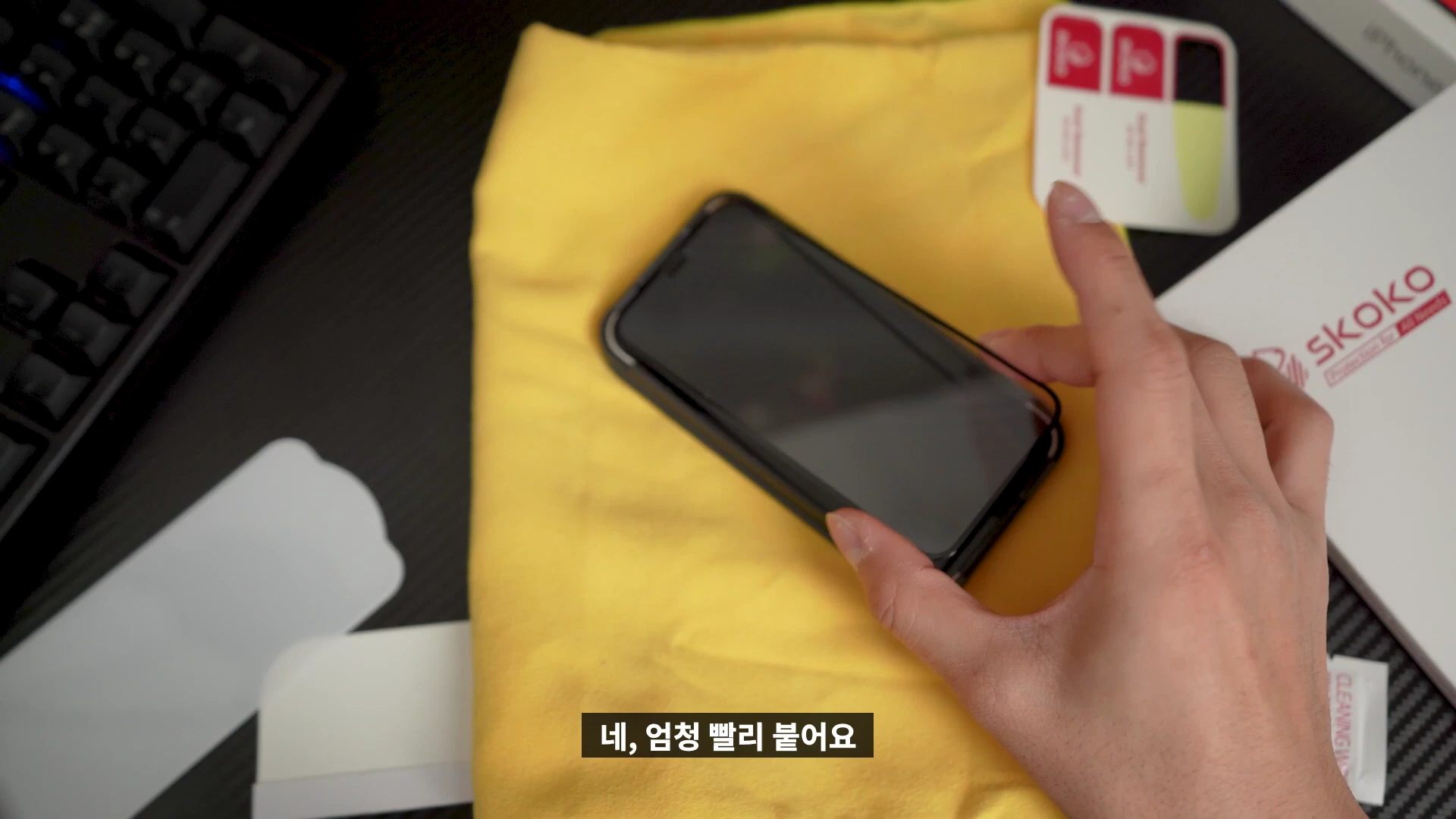 스마트폰 위에 강화유리 필름을 부착하고 있는 손과 주변의 부착 도구들