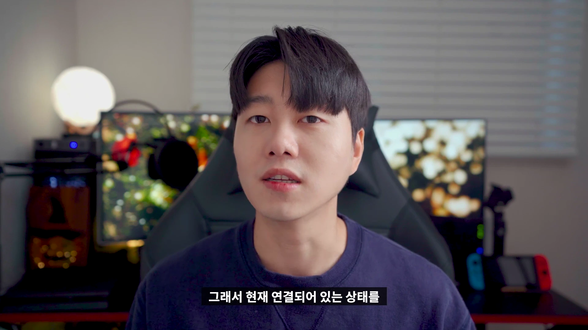 실내에서 카메라를 정면으로 응시하며 이야기하는 남성