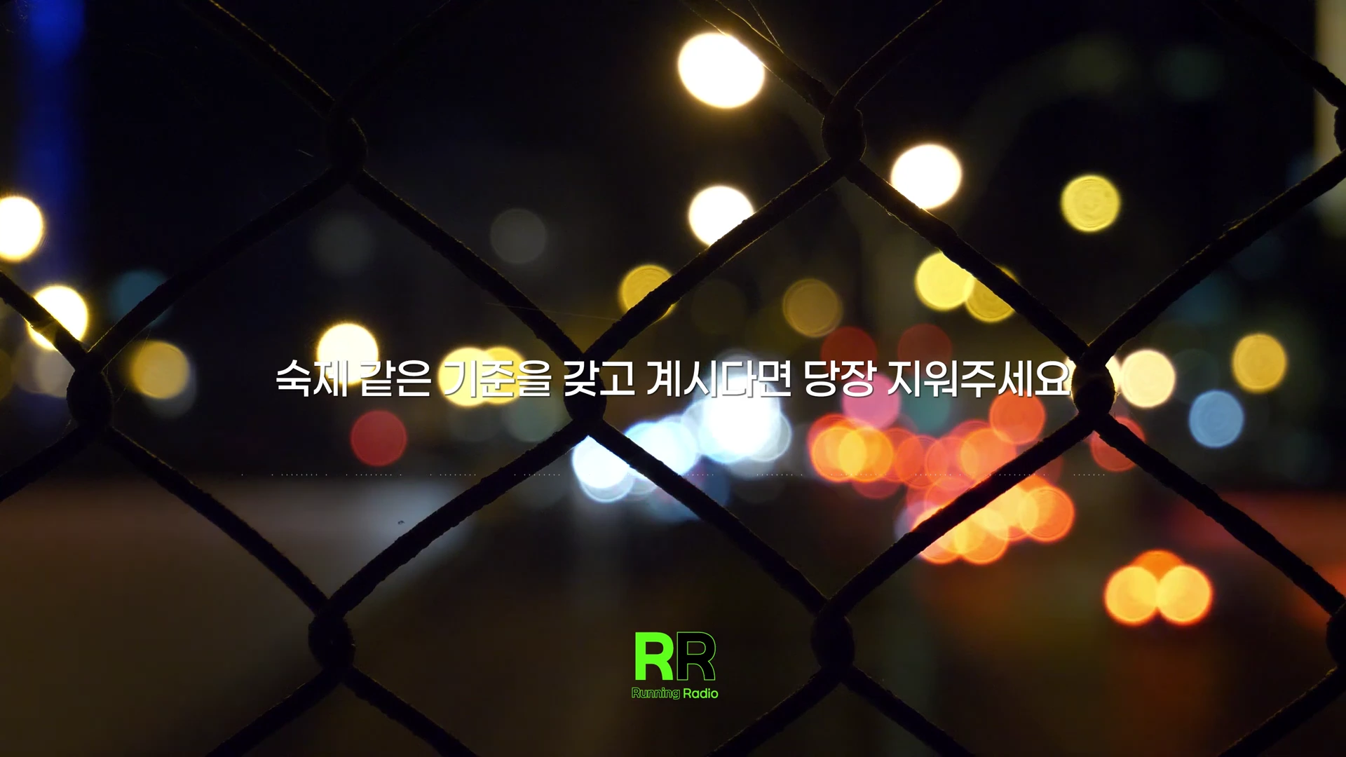 철망 너머로 밤거리의 흐릿한 조명들이 보이고, 그 위에 흰색 자막이 적혀 있습니다.