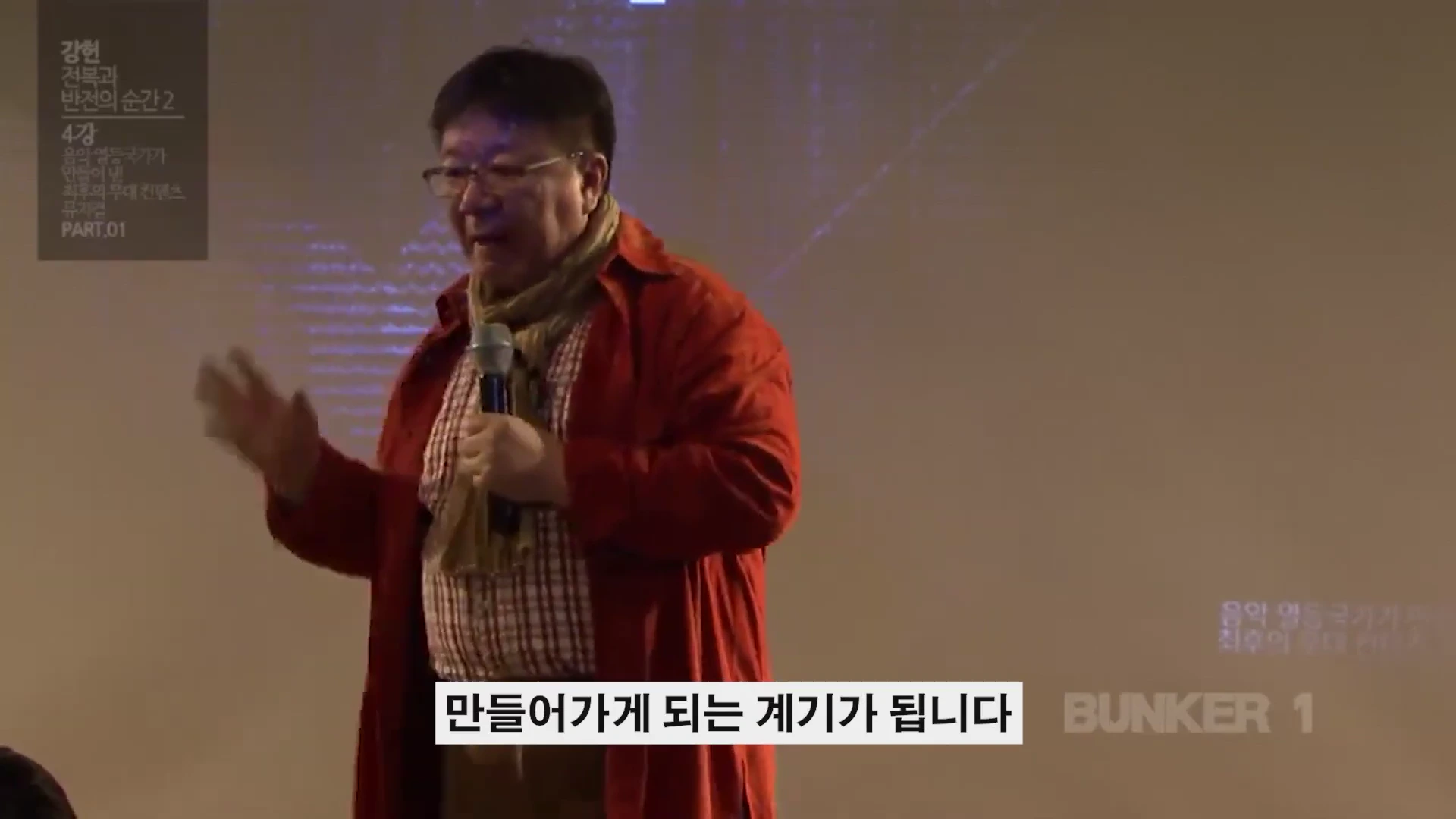강연장에서 마이크를 들고 손짓하며 이야기하는 중년 남성 강연자