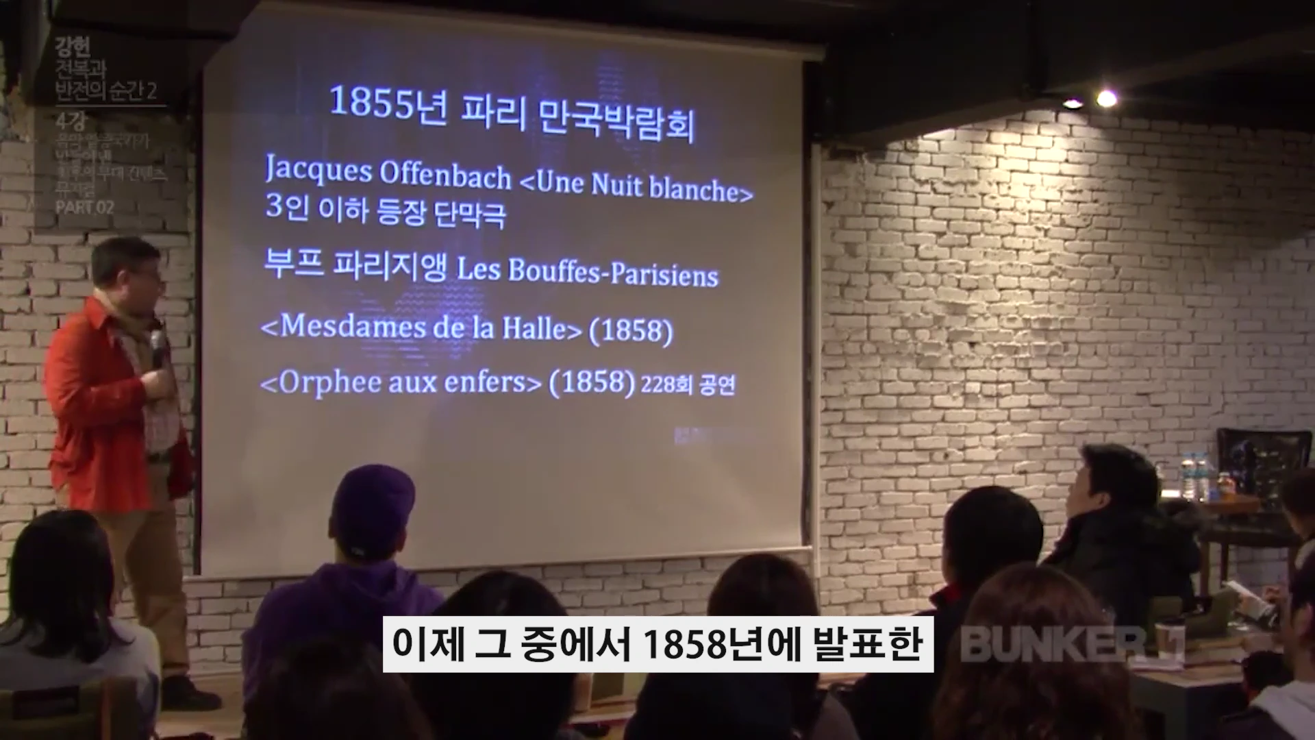 강연자가 스크린에 1855년 파리 만국박람회와 오펜바흐의 작품 정보가 적힌 발표 자료를 띄워놓고 청중 앞에서 설명하고 있다.