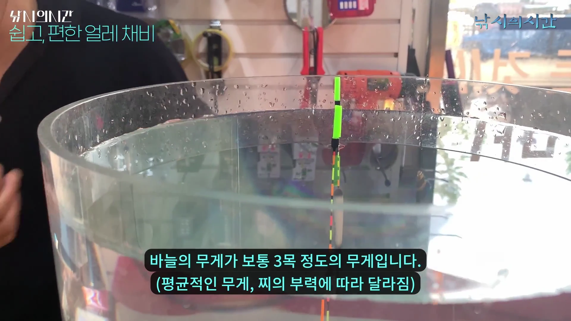 투명한 수조 안에 낚시찌가 수직으로 떠 있고, 화면 하단에 바늘 무게와 찌 부력에 관한 설명 자막이 표시된 모습