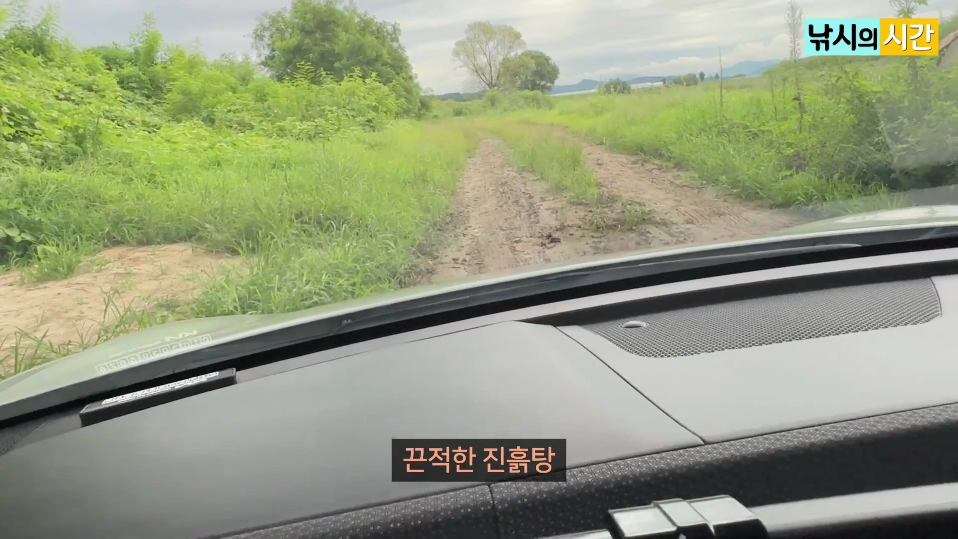 차량 내부에서 바라본 풀이 무성한 비포장 진흙길과 주변 풍경