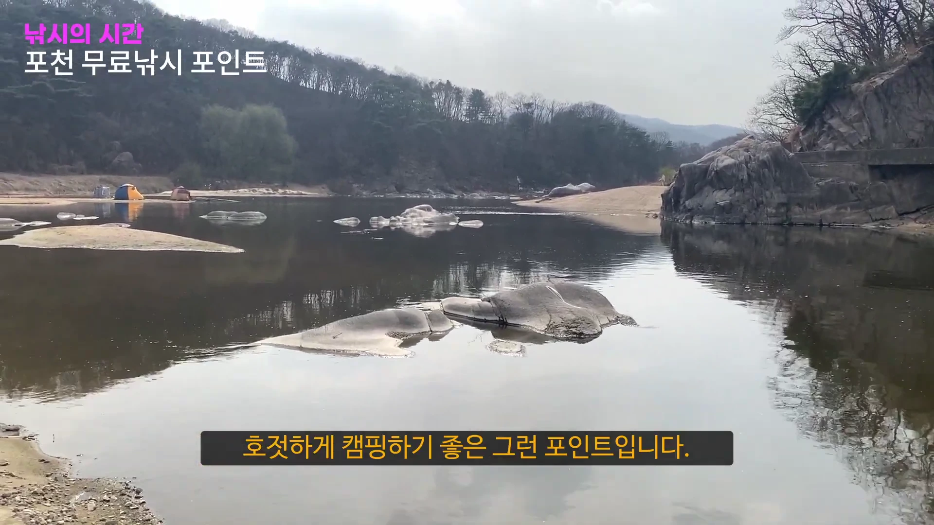 산으로 둘러싸인 고요한 강가와 모래사장, 멀리 텐트가 보이는 풍경