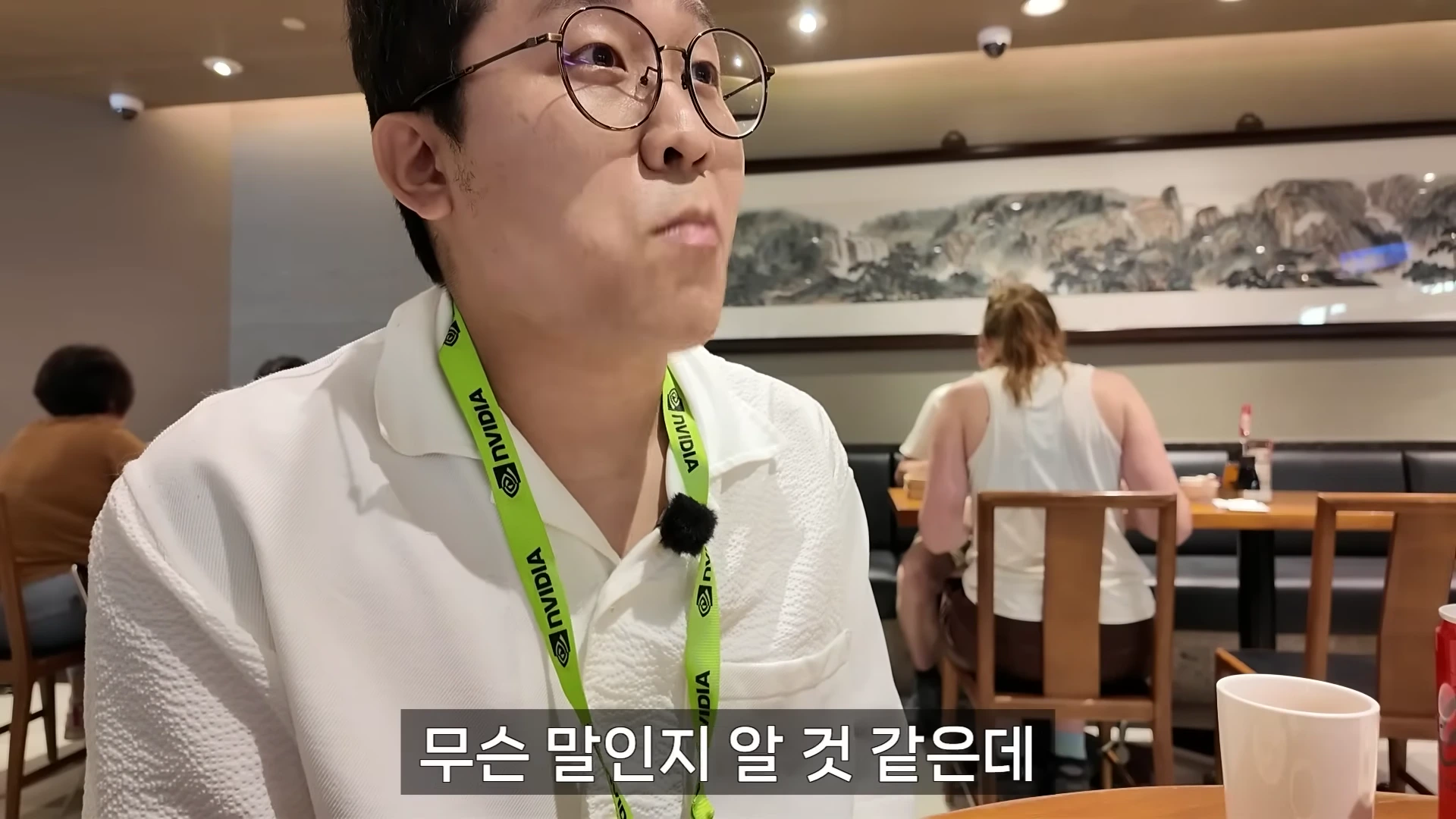 안경을 쓴 남성이 엔비디아 로고가 새겨진 목걸이를 걸고 식당에서 대화하는 모습