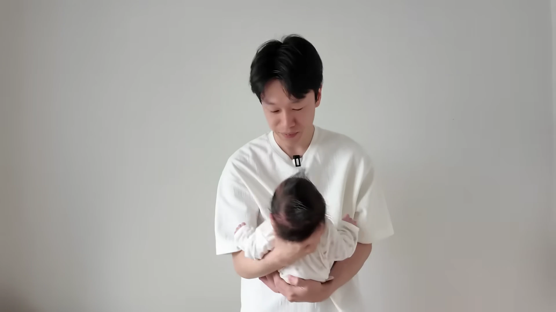 흰색 티셔츠를 입은 남성이 아기를 조심스럽게 안고 있는 모습