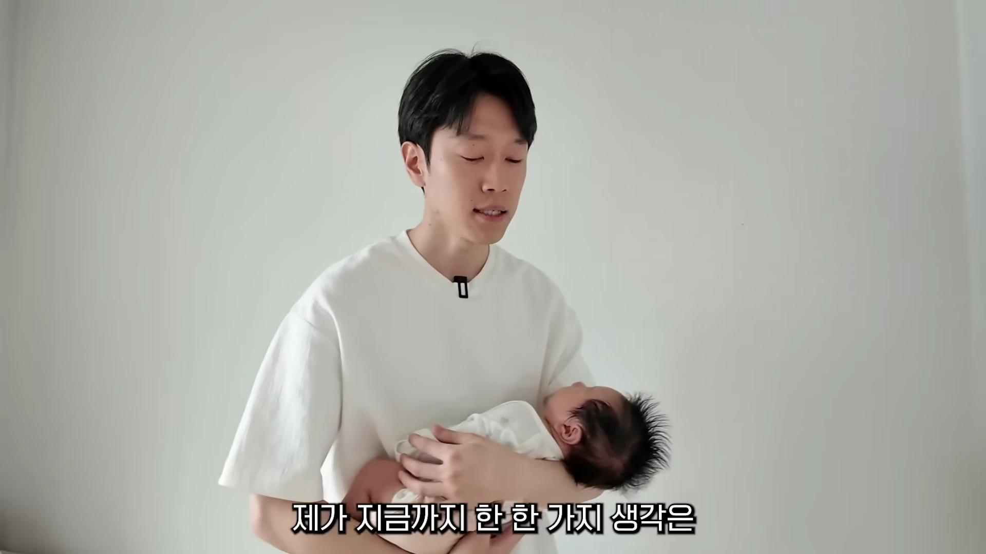 흰색 티셔츠를 입은 남성이 갓난아기를 품에 안고 이야기를 나누고 있다.