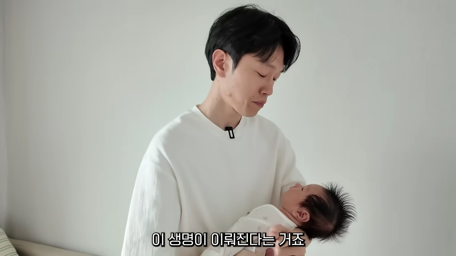 흰색 상의를 입은 남성이 갓난아기를 조심스럽게 안고 있는 모습