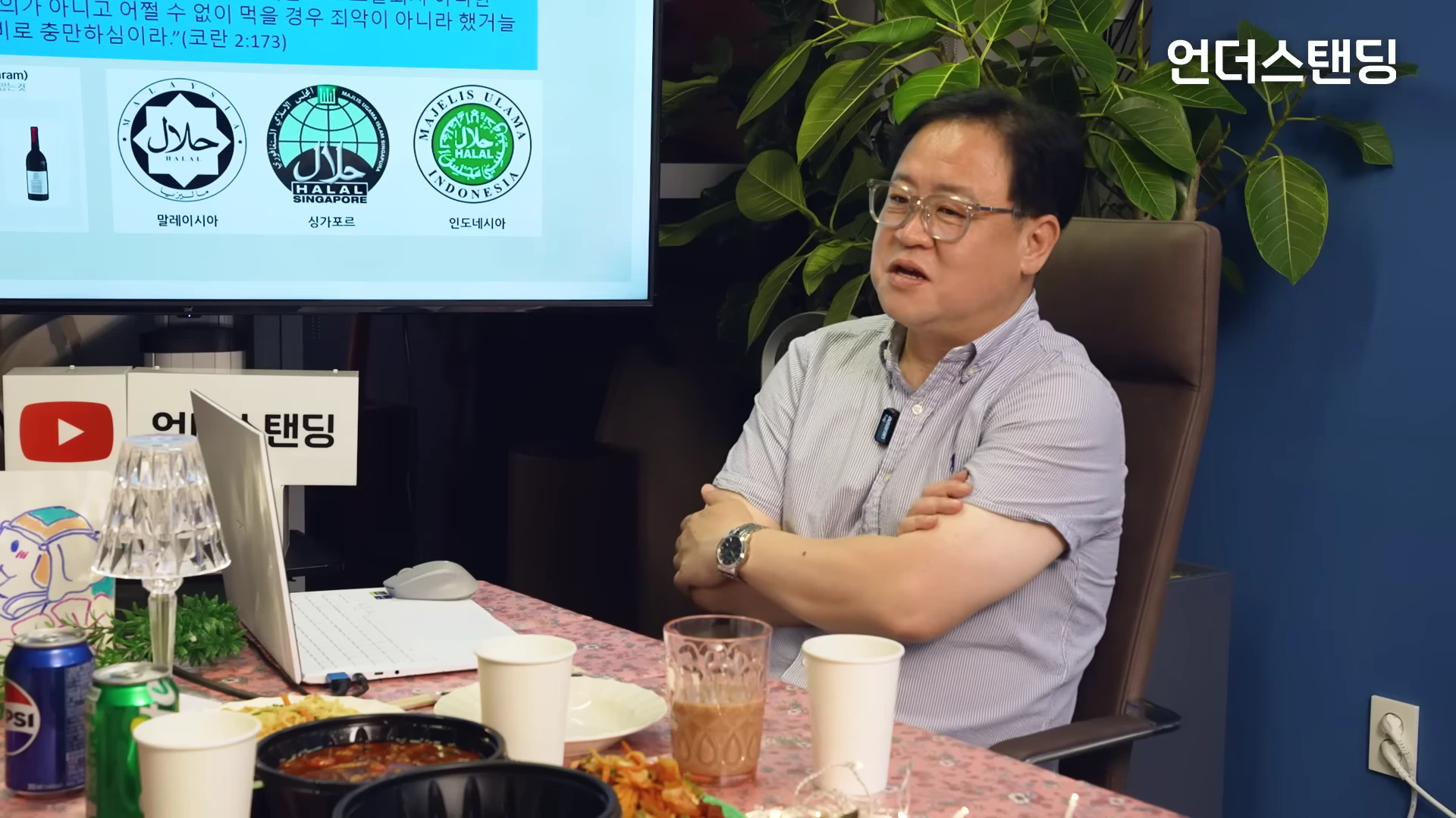 스튜디오에서 팔짱을 끼고 앉아 대담을 나누는 중년 남성과 뒤편의 할랄 인증 마크가 담긴 화면