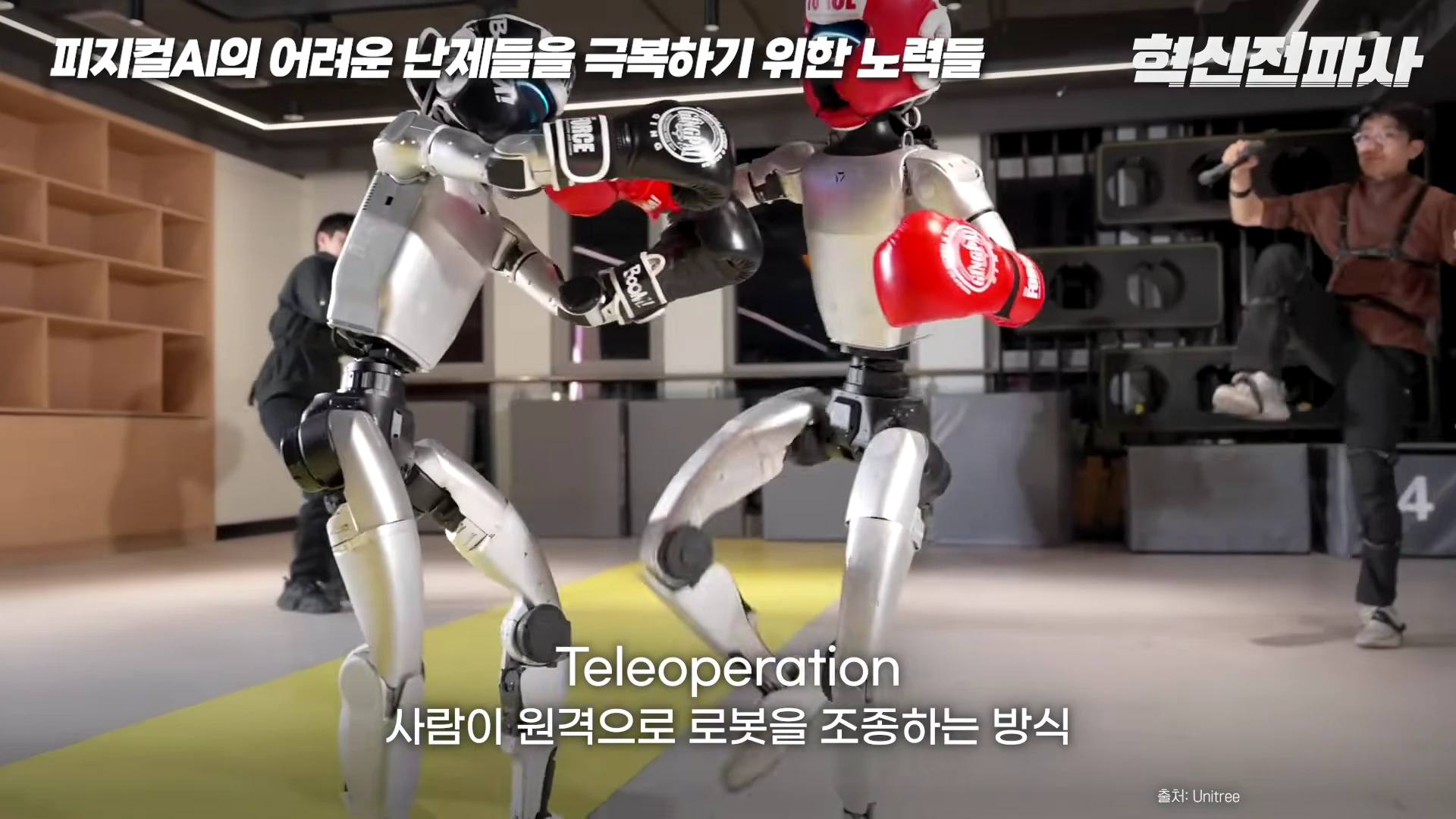 복싱 글러브를 낀 두 대의 휴머노이드 로봇이 실내에서 대련하고 있고, 뒤편에서 사람이 원격 조종 장치를 착용하고 움직이는 모습