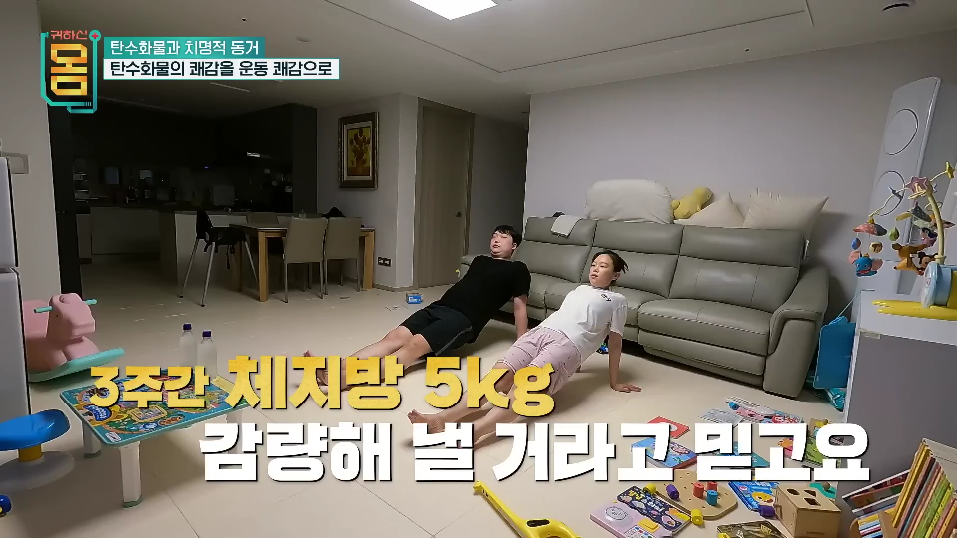 거실 바닥에서 부부가 나란히 앉아 팔을 뒤로 짚고 다리를 뻗은 채 근력 운동을 하고 있는 모습