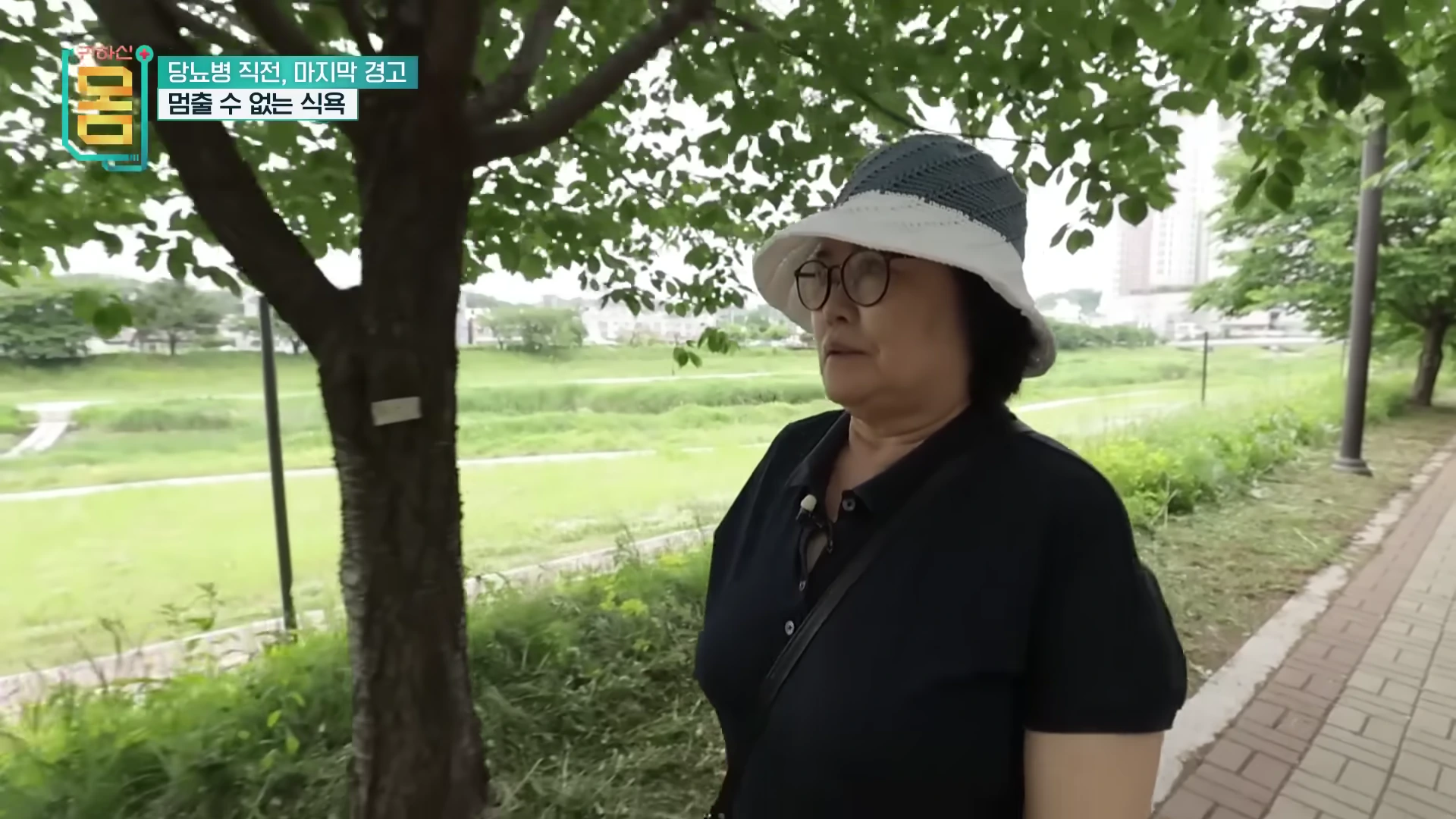 공원 산책로에서 모자를 쓰고 안경을 쓴 중년 여성이 걷고 있는 모습