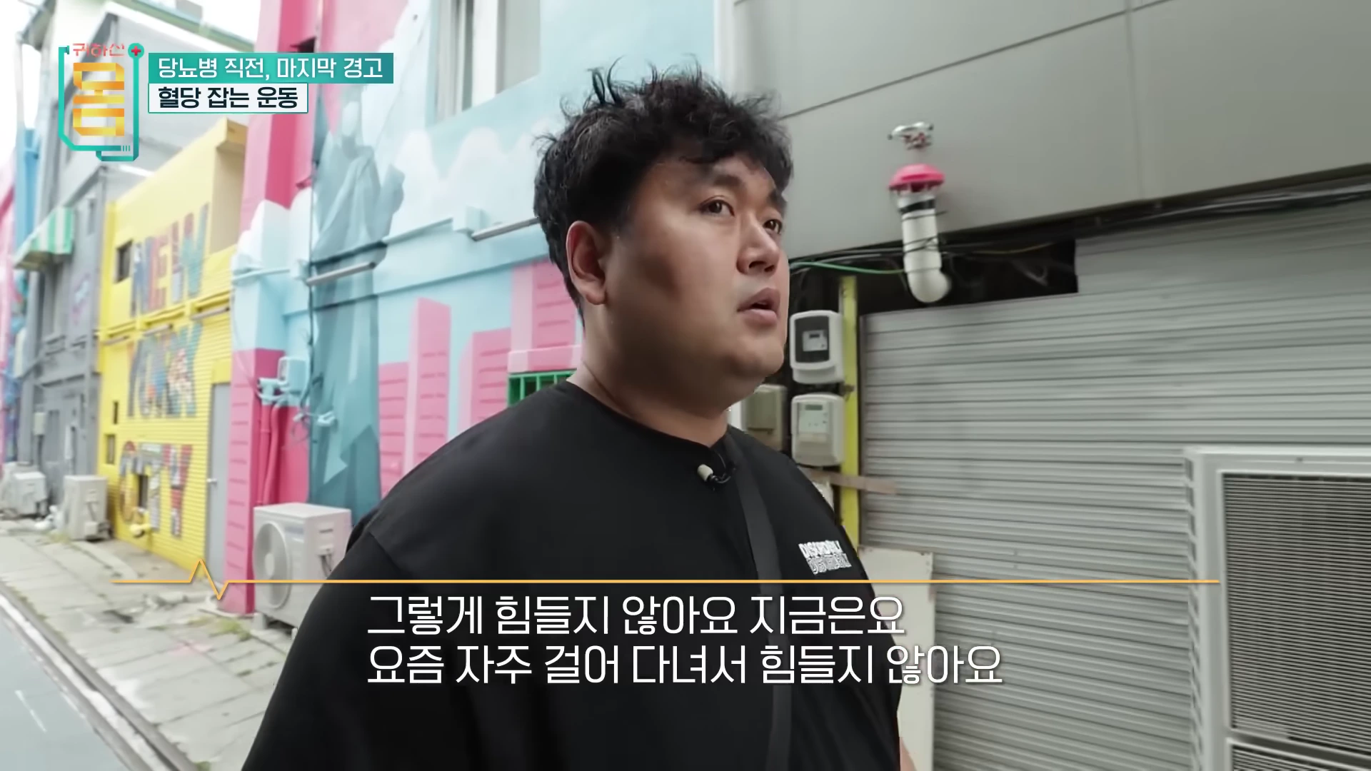 검은색 티셔츠를 입은 남성이 골목길에서 인터뷰하는 모습