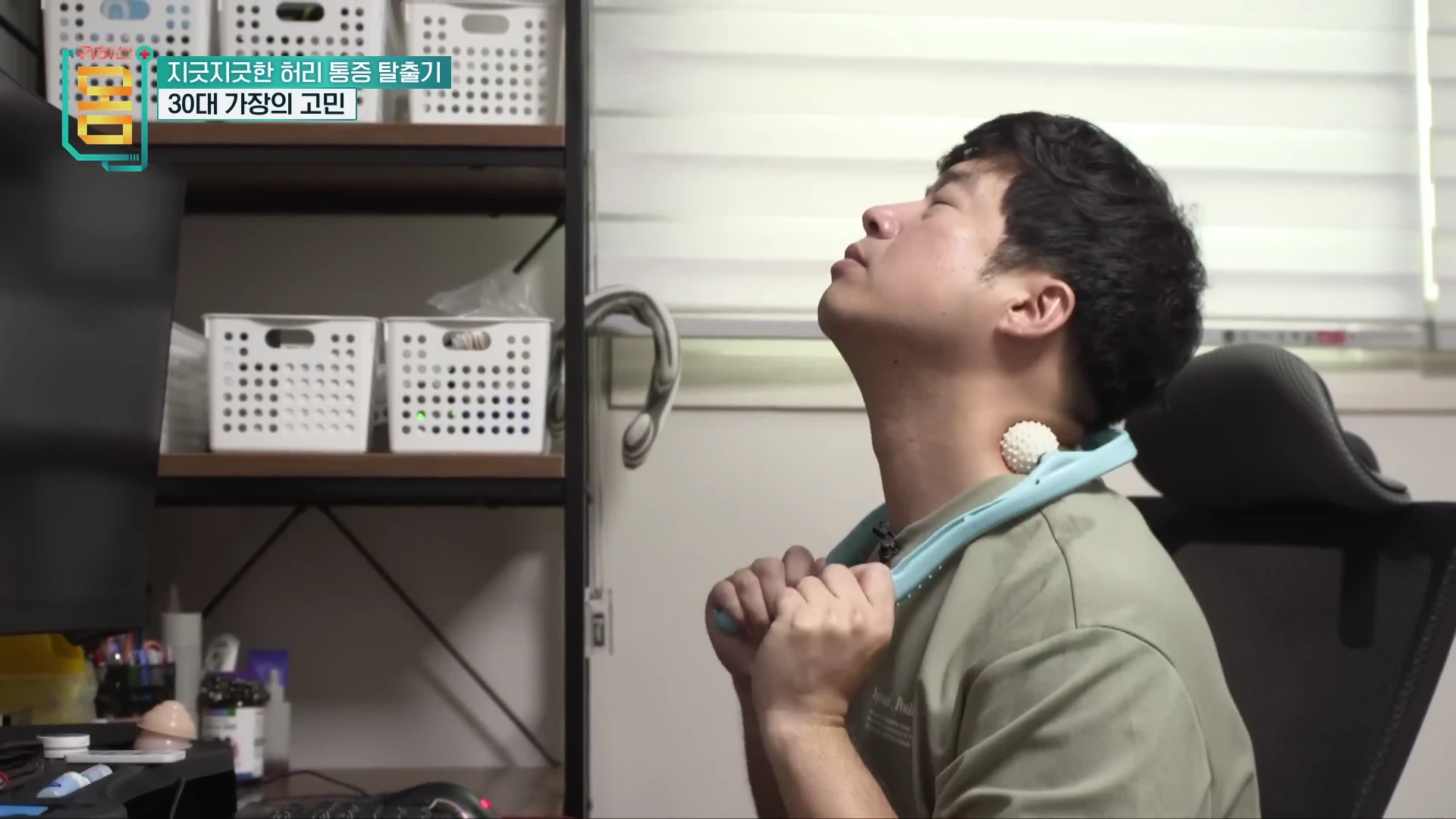 컴퓨터 앞에 앉아 목 뒤에 마사지 도구를 대고 고통스러운 표정으로 몸을 푸는 남성