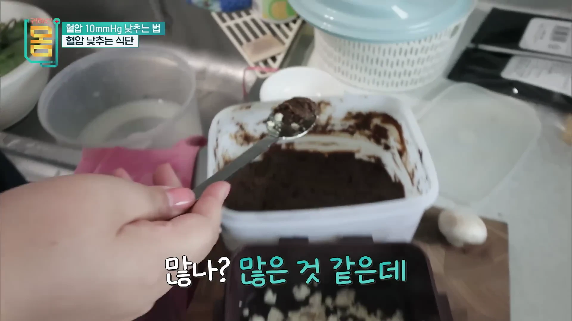 주방에서 한 사람이 숟가락으로 된장을 조금 떠서 양을 확인하고 있는 모습