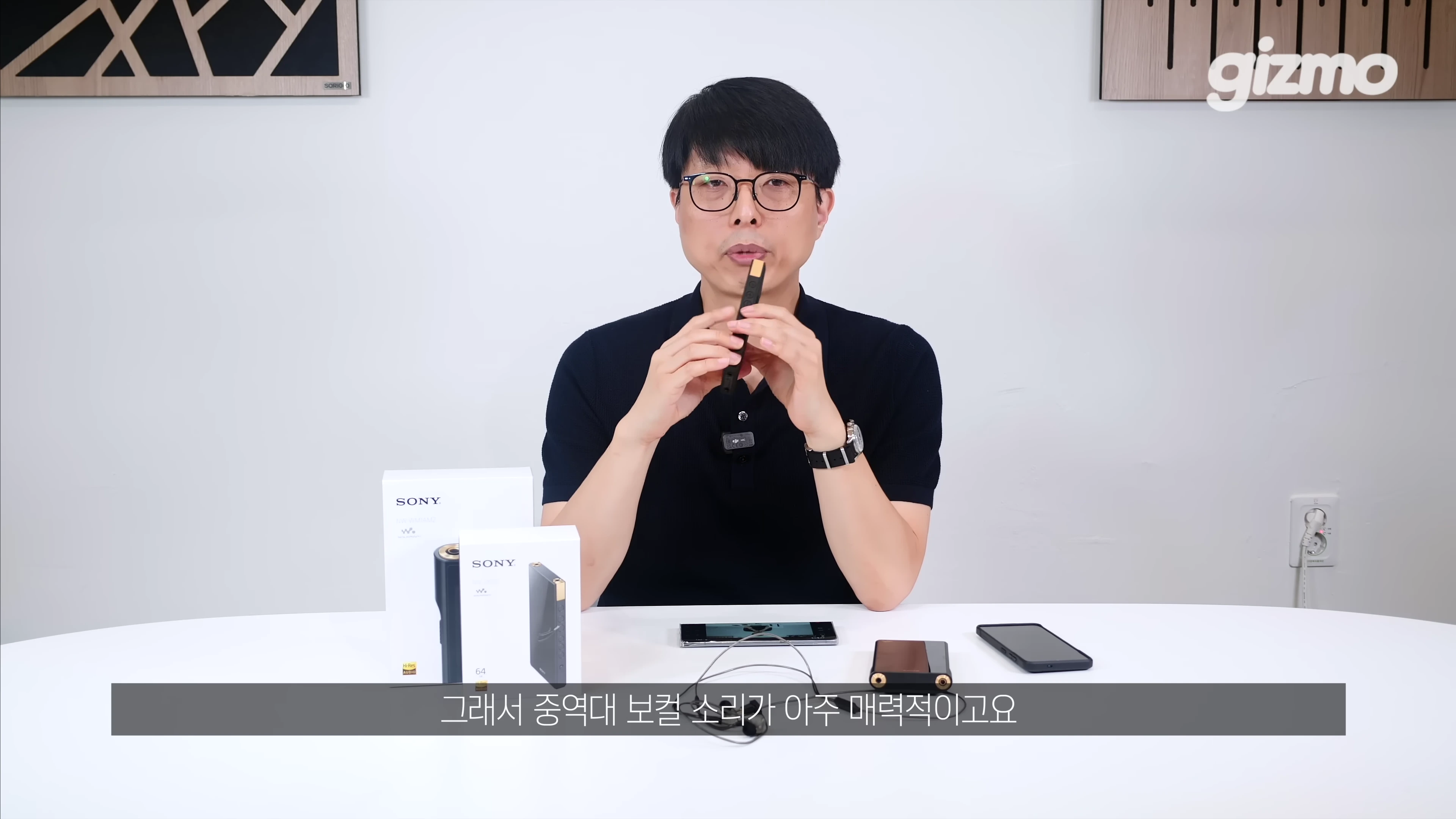 안경을 쓴 남성이 스튜디오 테이블에 앉아 소니 DAP 기기를 손에 들고 설명하고 있다.