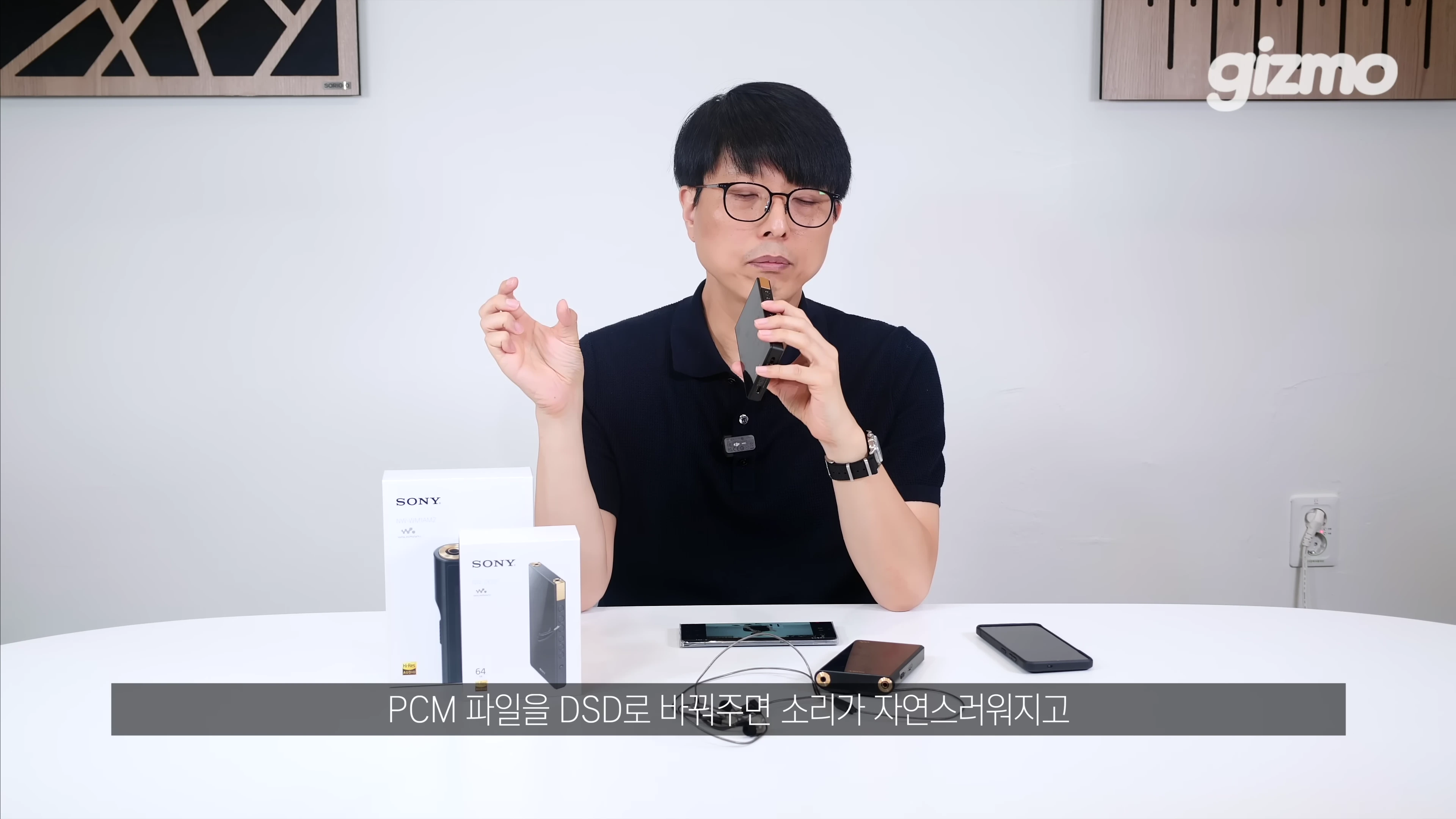 안경을 쓴 남성이 테이블 앞에 앉아 소니 디지털 오디오 플레이어를 손에 들고 설명하는 모습