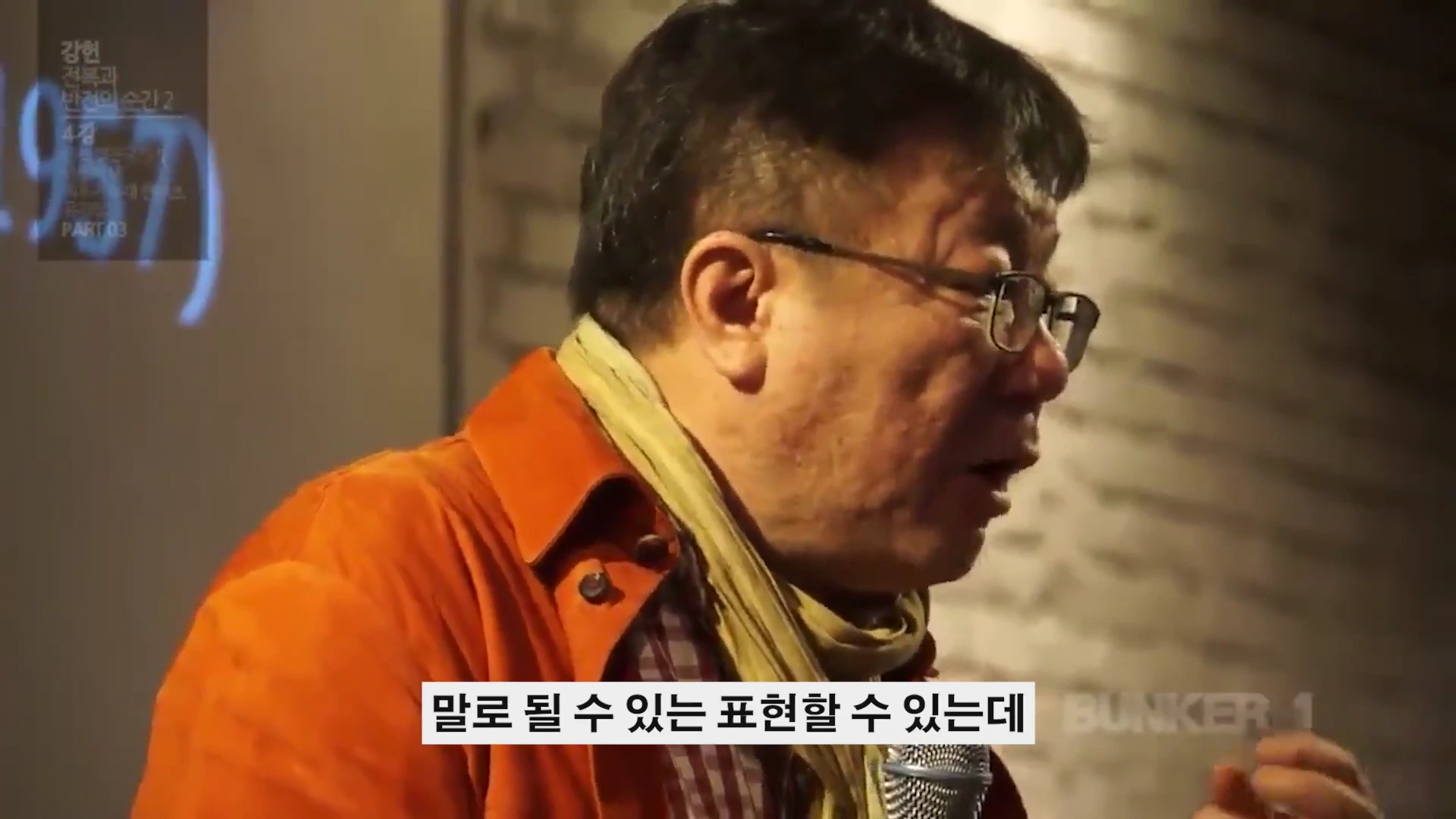 안경을 쓴 중년 남성이 주황색 재킷을 입고 강연하는 모습이 담긴 영상 캡처 화면