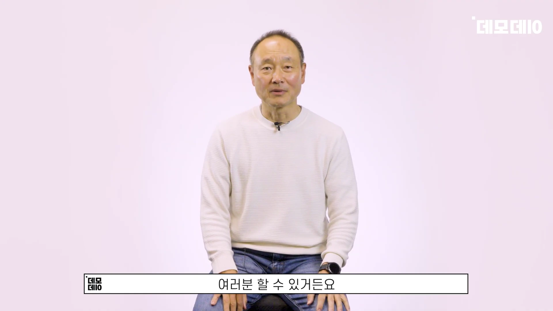 흰색 니트를 입은 중년 남성이 밝은 배경 앞에서 정면을 응시하며 이야기하는 모습